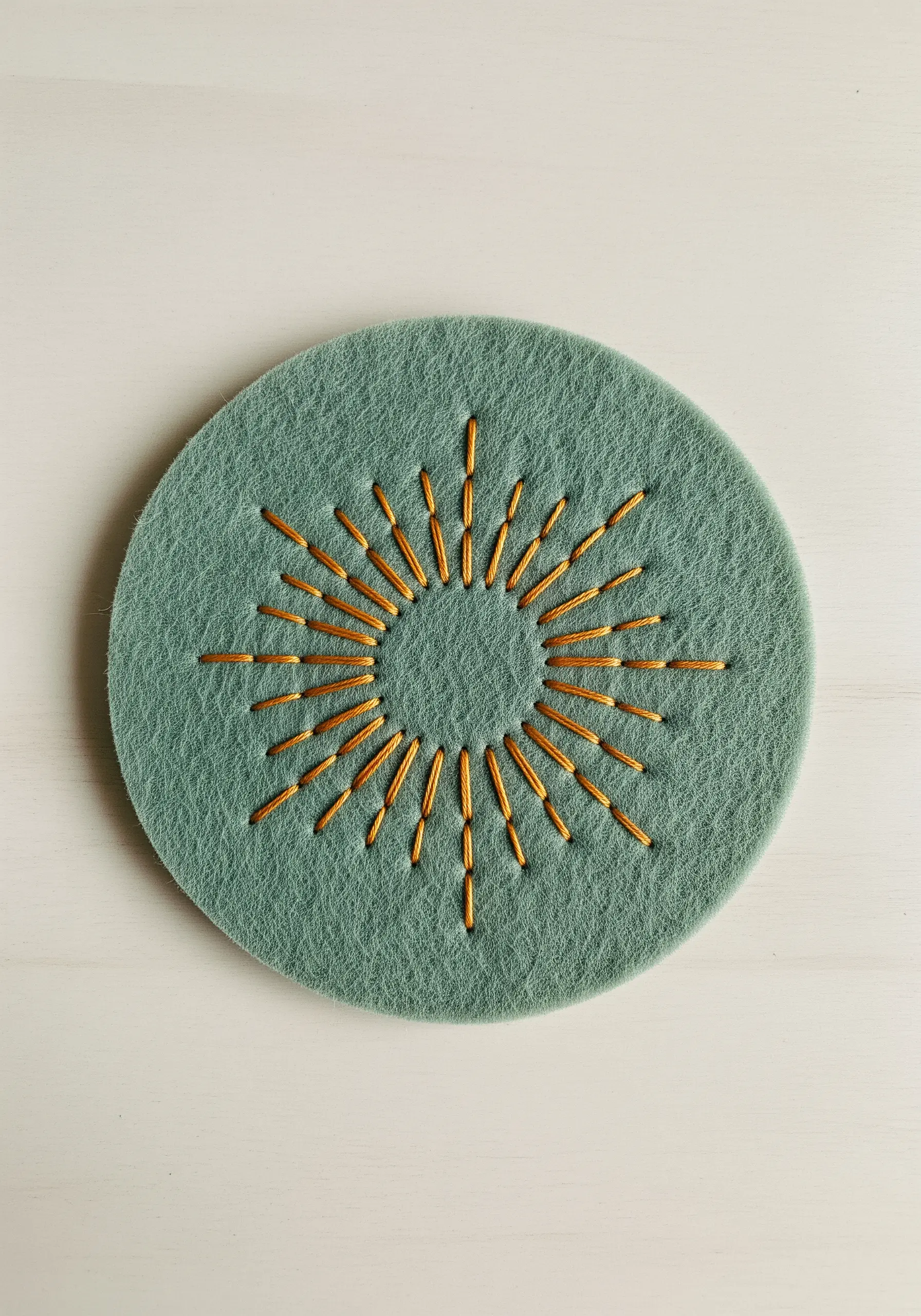 A sunburst motif made with gold bugle beads and thread on a round green felt coaster.