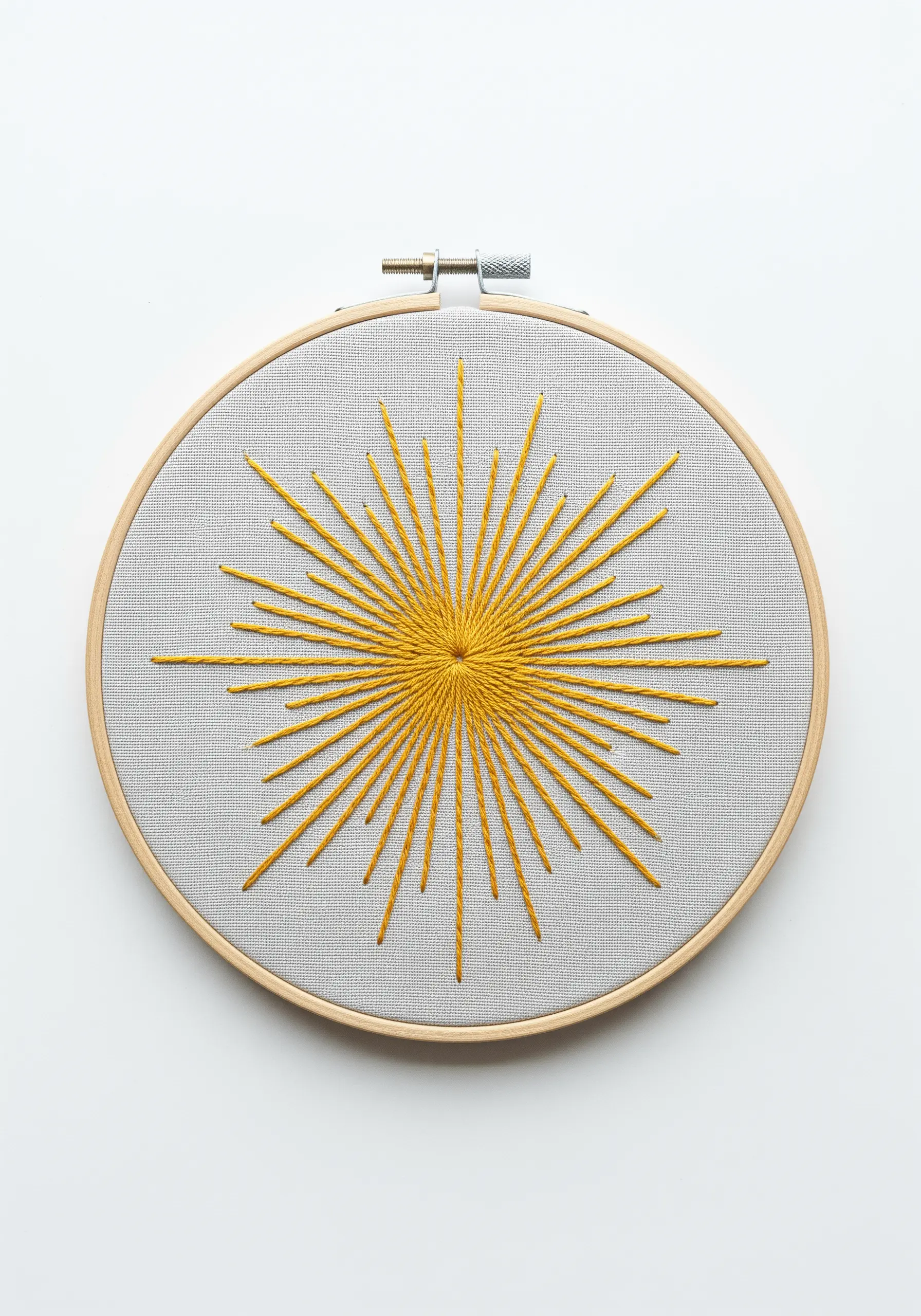A vibrant yellow sunburst embroidered with radiating straight stitches in a wooden hoop.