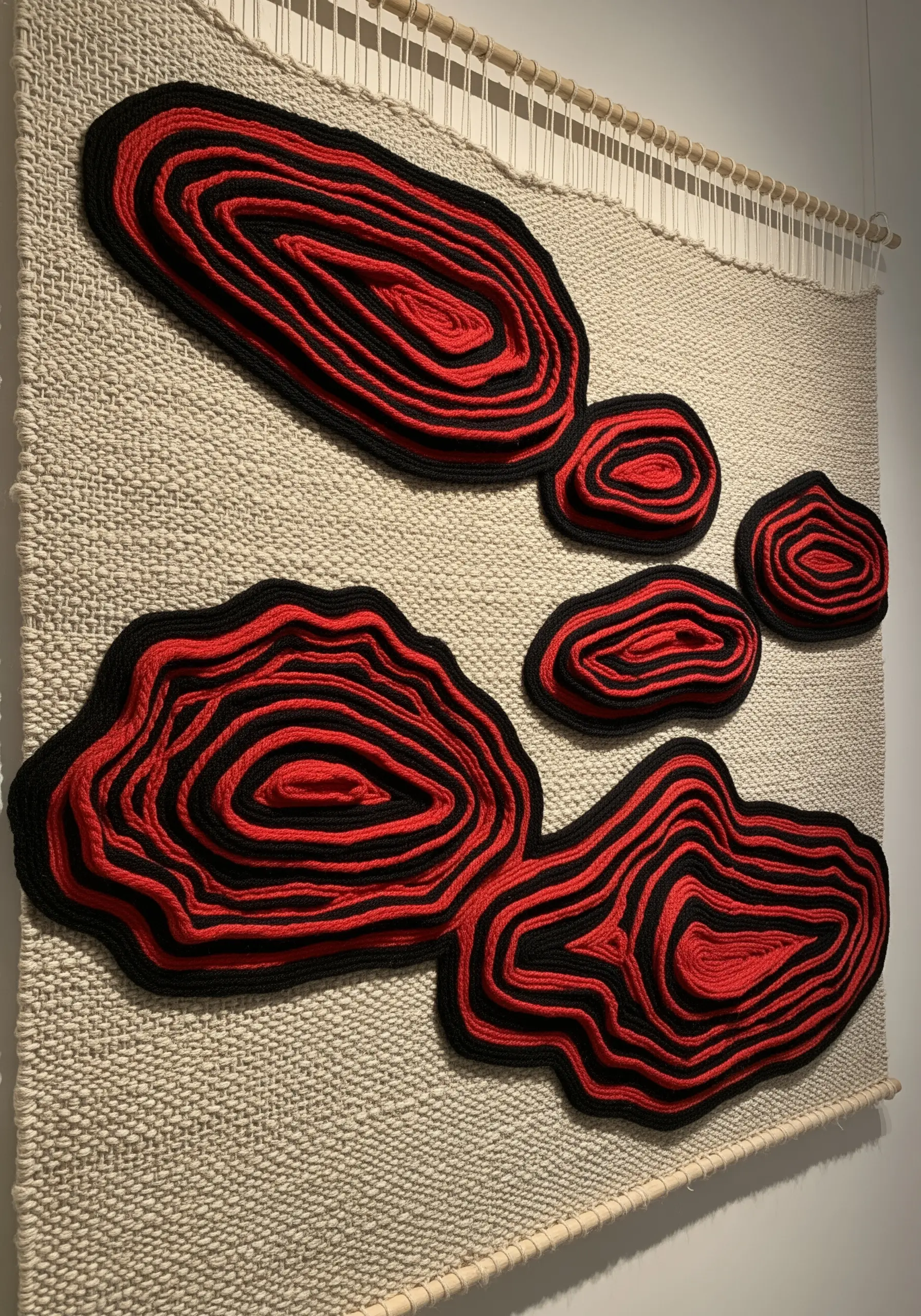 Black and red layered yarn appliqué forms stitched onto a neutral woven wall hanging.