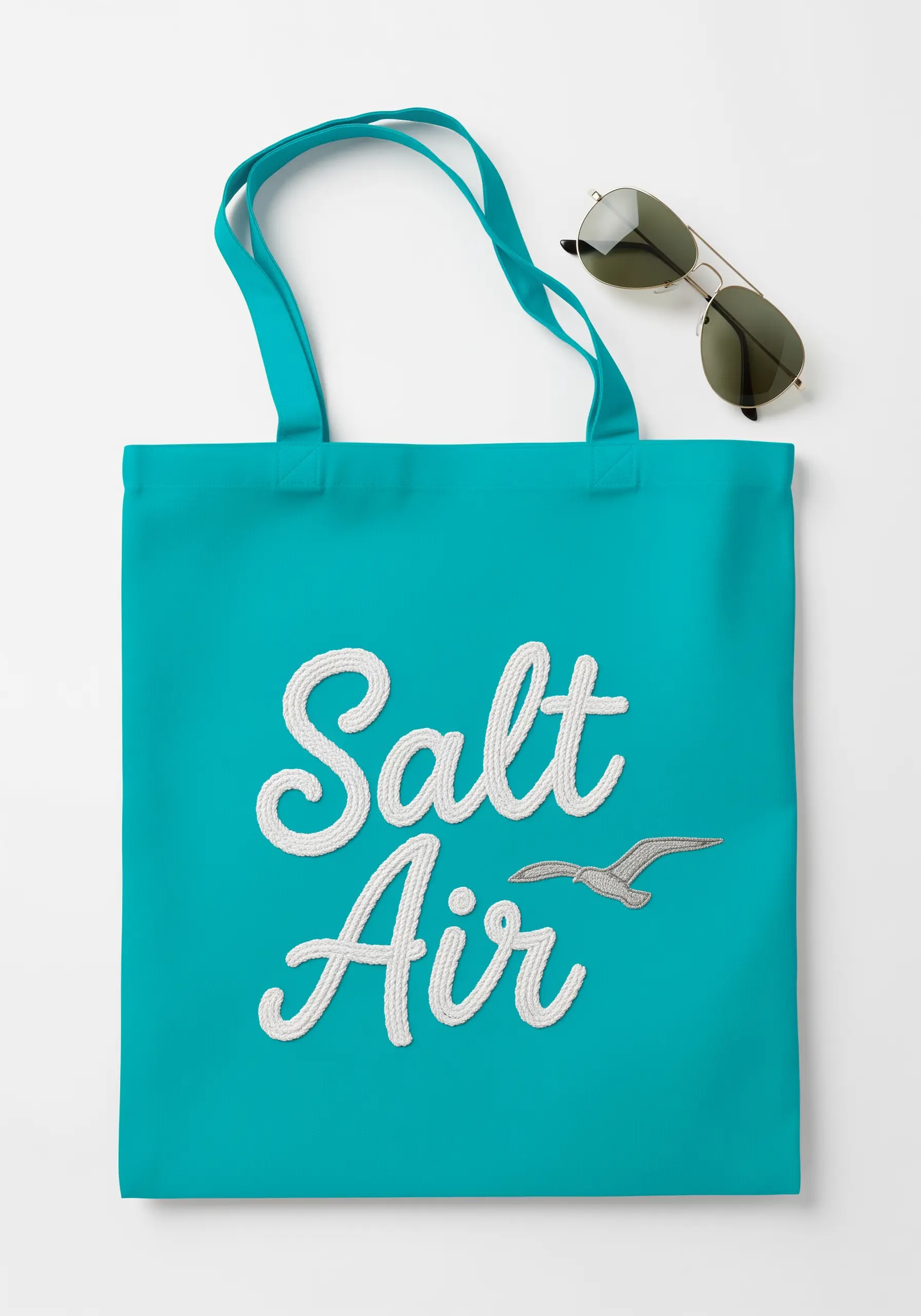 The words 'Salt Air' embroidered in a raised white script on a bright turquoise tote bag.
