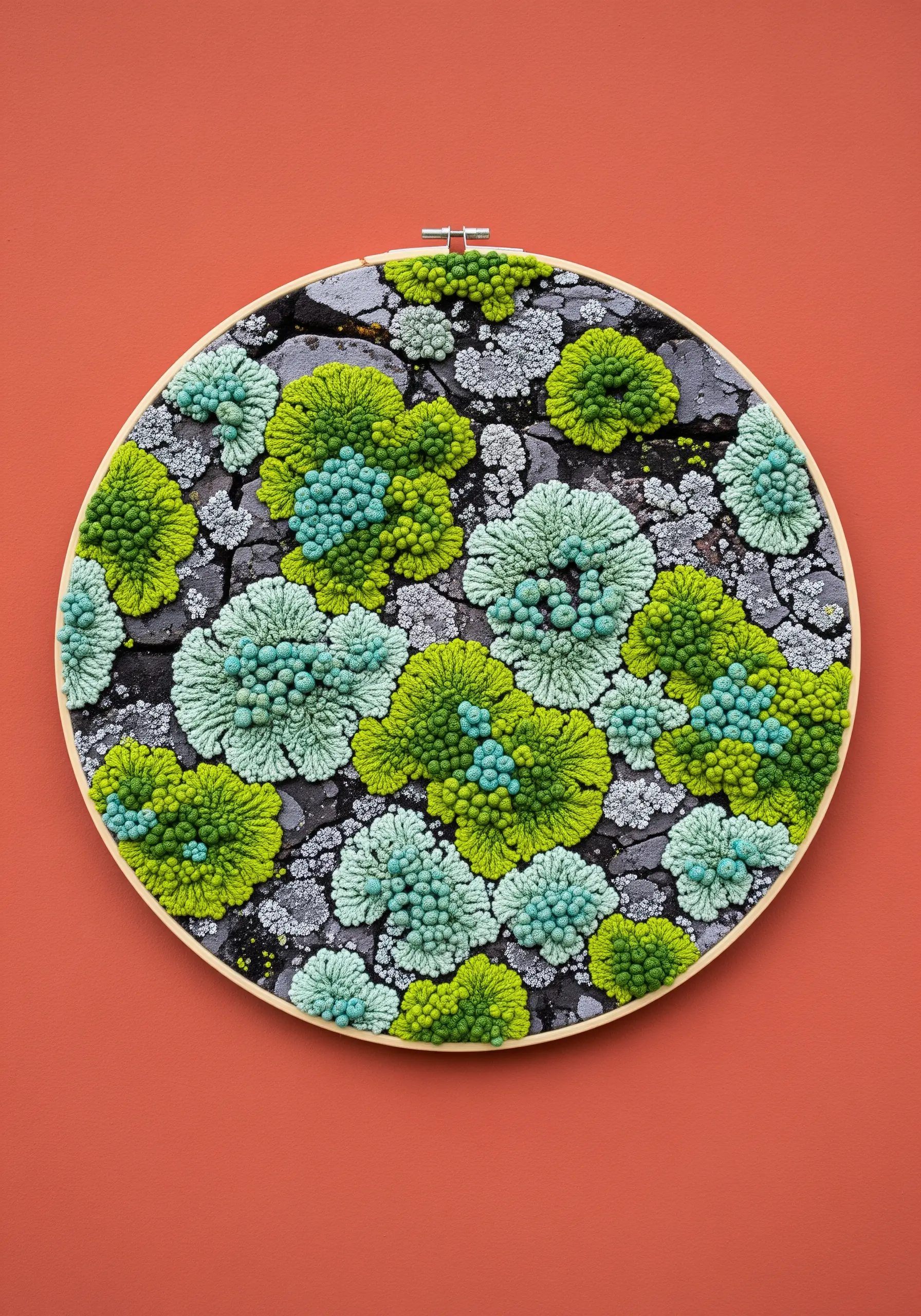A detailed embroidery hoop filled with clustered French knots in green and seafoam, resembling lichen on rock.