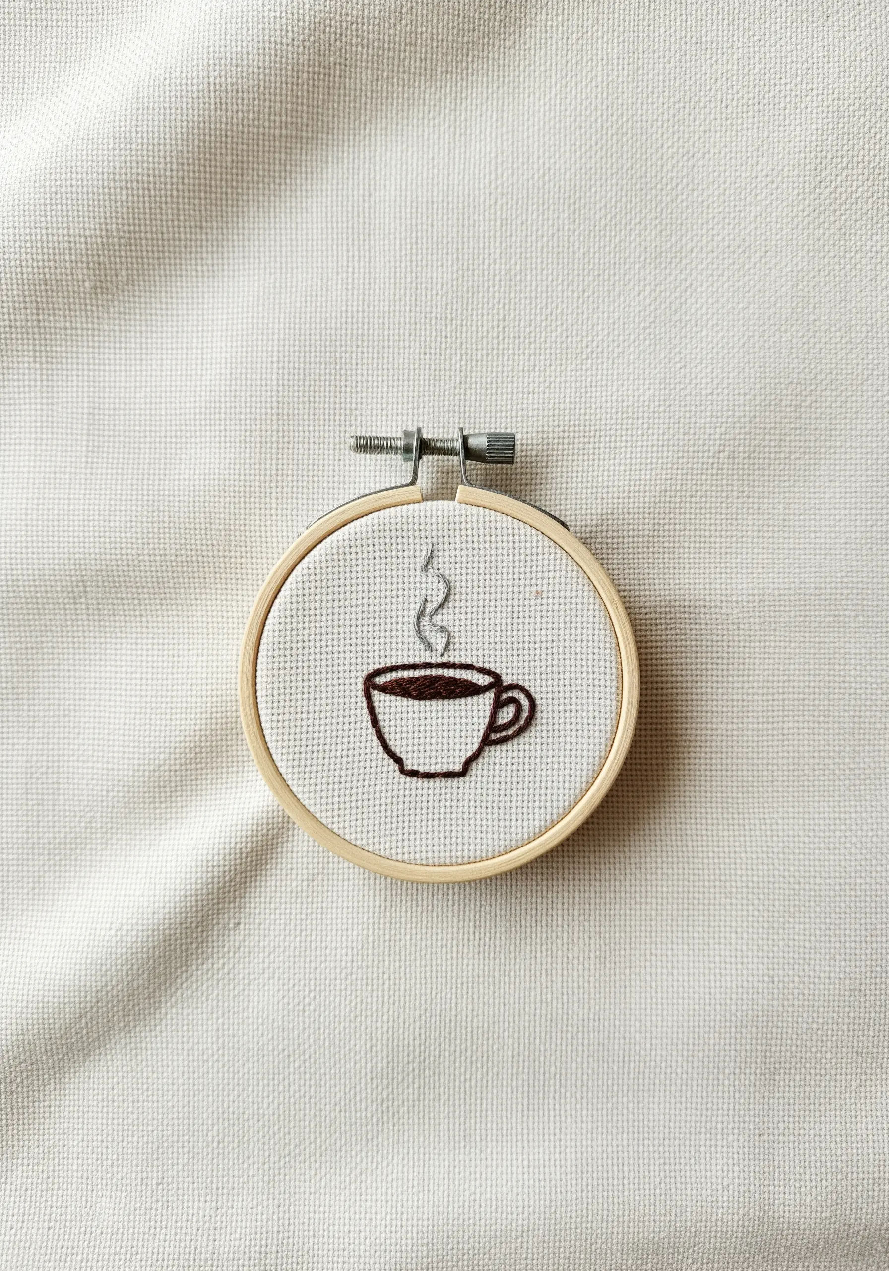 A tiny embroidered coffee cup with steam, stitched in a small hoop.