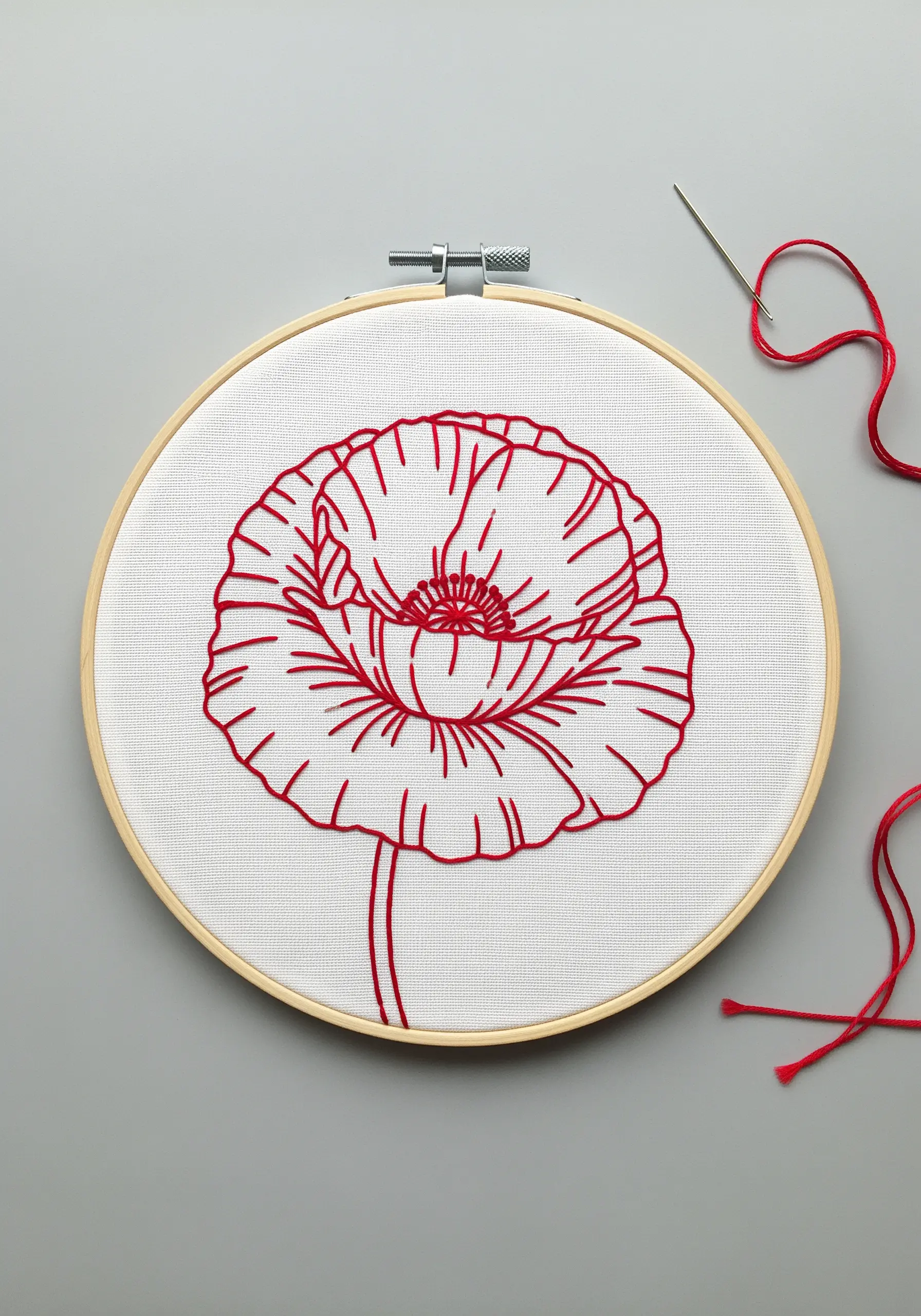 Red line art embroidery of a poppy on white fabric, showing clean, continuous lines.