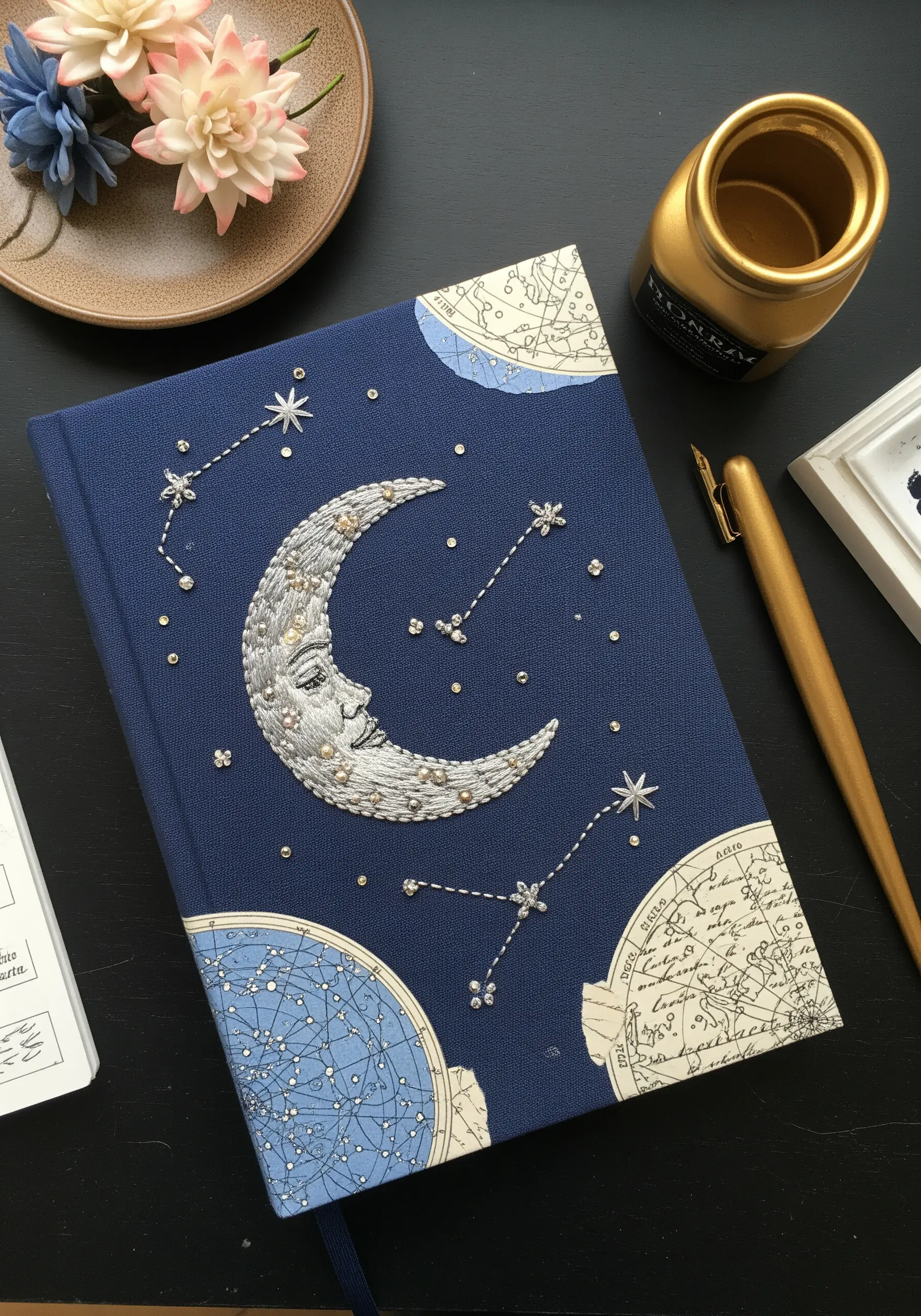 Embroidered celestial moon with silver thread and beads on a dark blue journal cover.