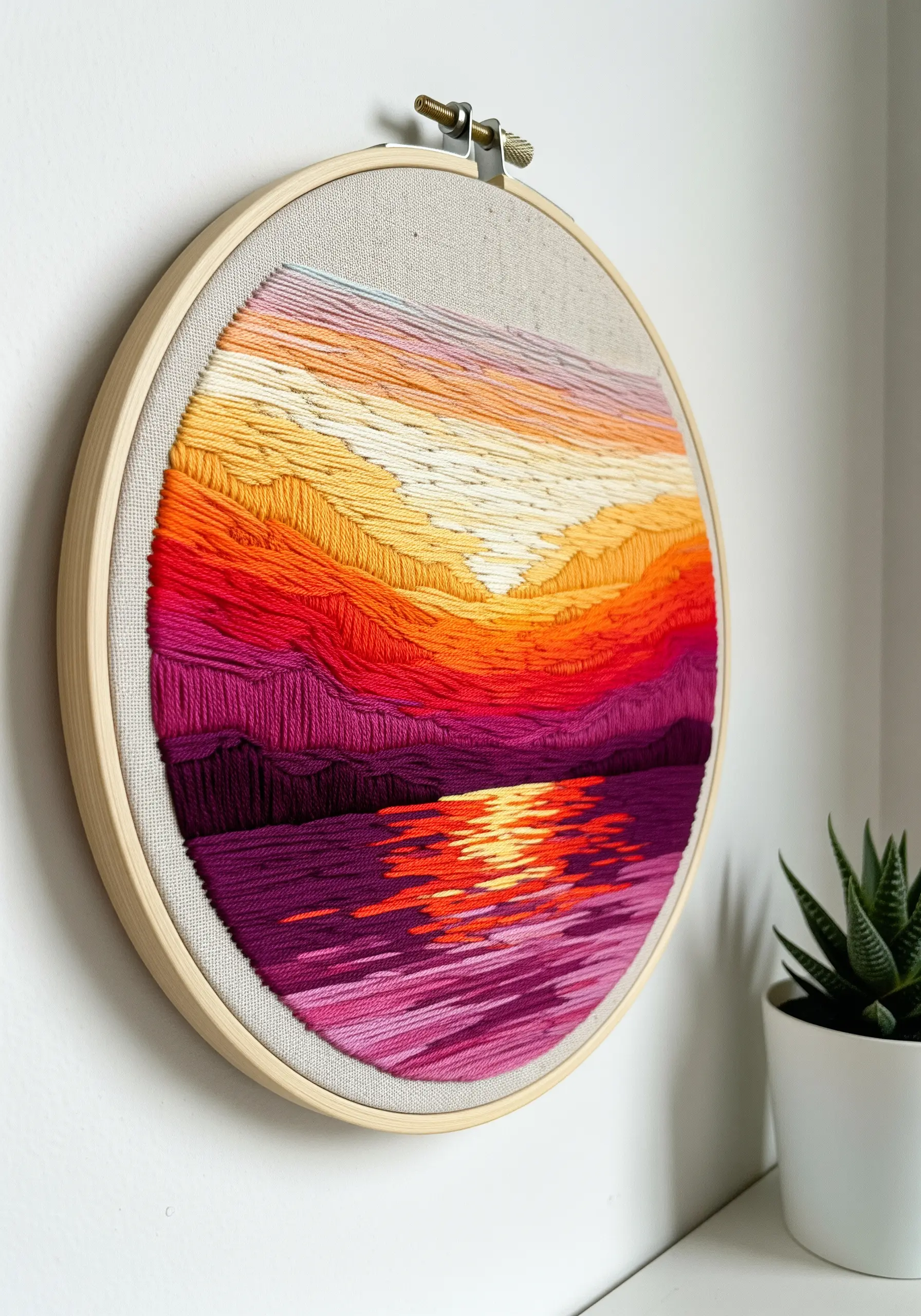 Embroidery hoop art of a vibrant sunset over water using satin stitch.