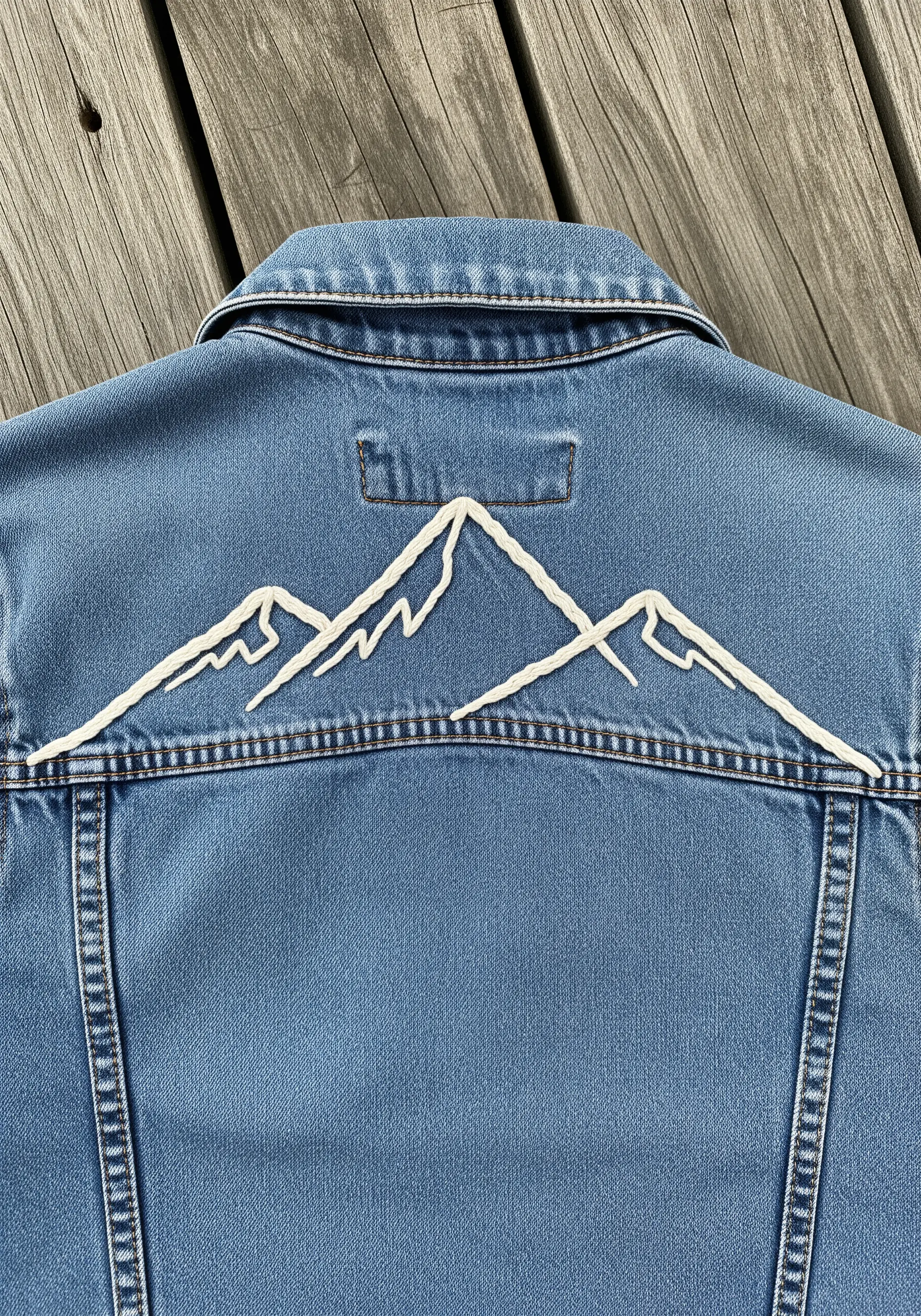 Bold white whipped stitch embroidery of a mountain range on the back of a denim jacket.