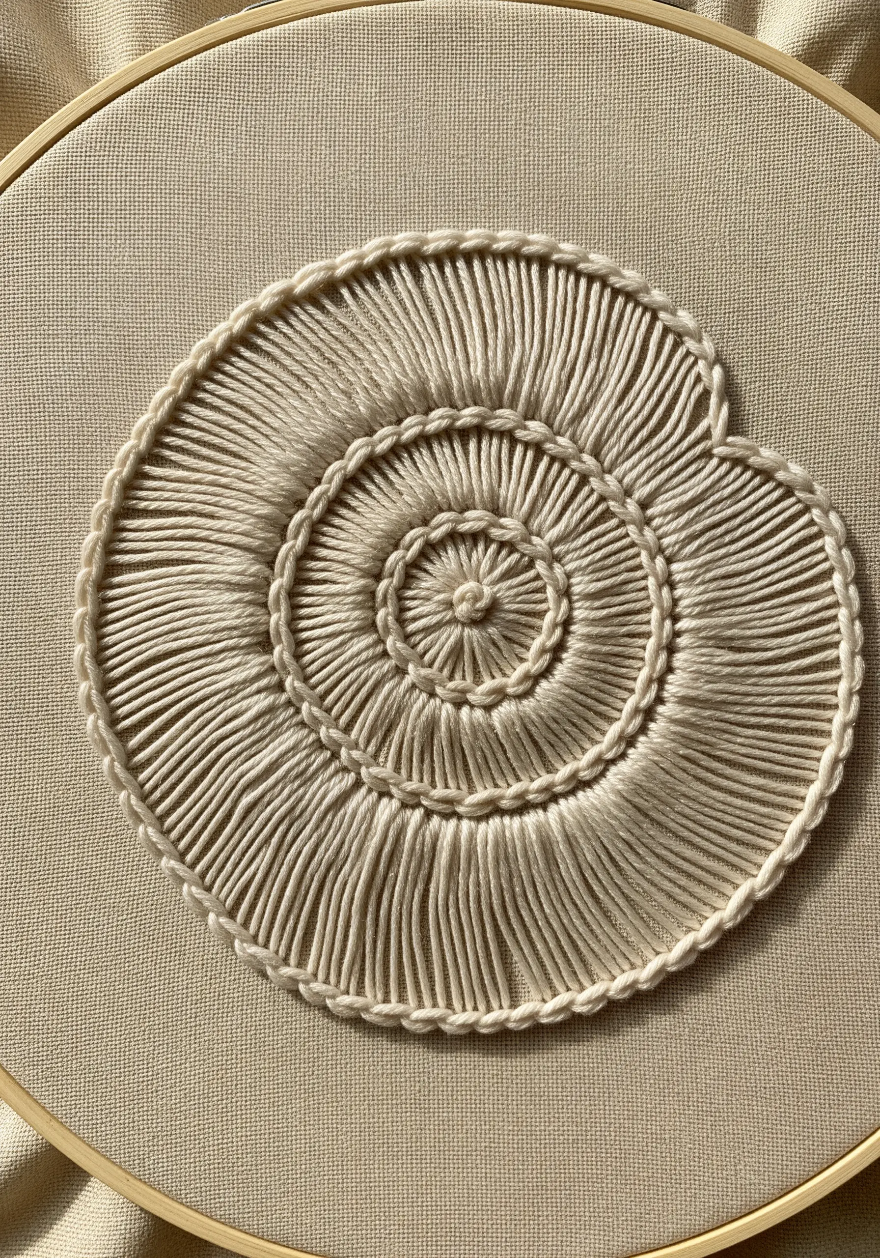 A seashell motif embroidered in off-white thread using raised stem stitch for a ridged texture.