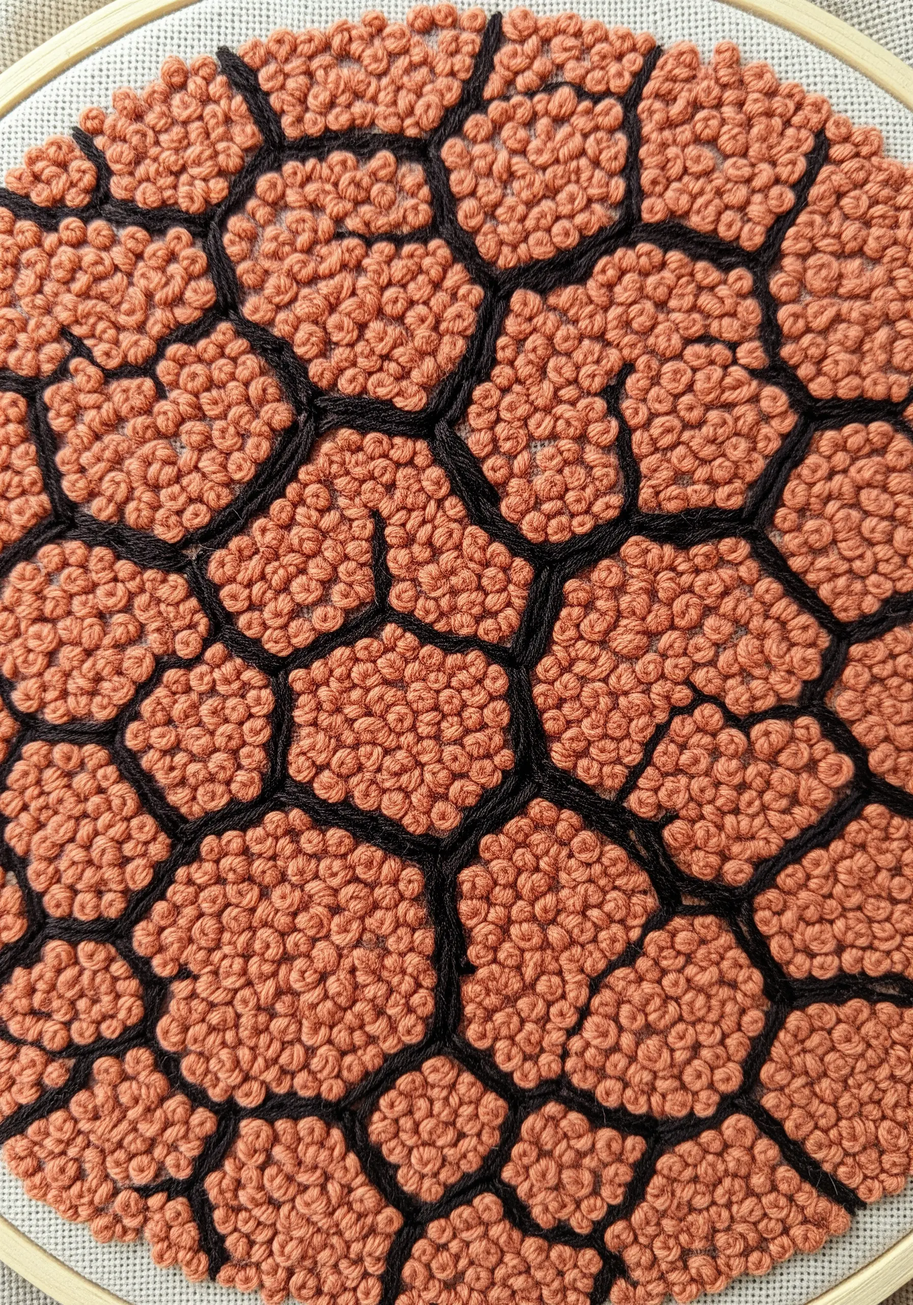 Close-up of terracotta-colored French knots filling honeycomb shapes outlined in black thread.