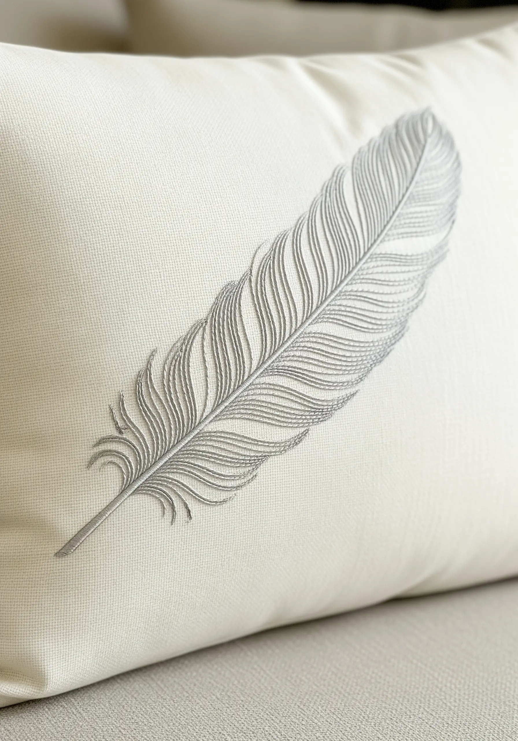 A delicate feather embroidered in fine grey thread on a smooth white cushion.