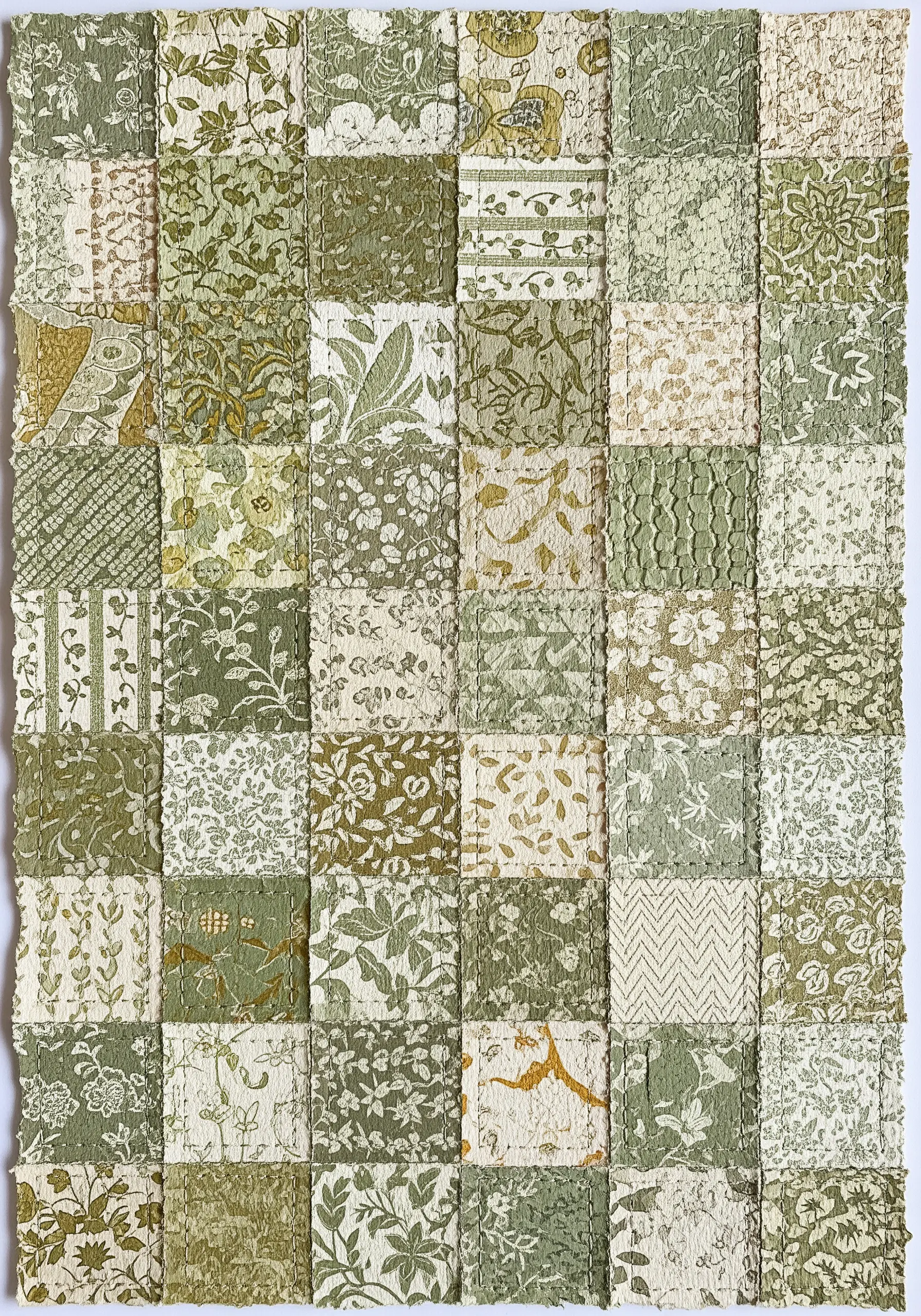 A patchwork collage made from squares of green and cream patterned paper stitched together.