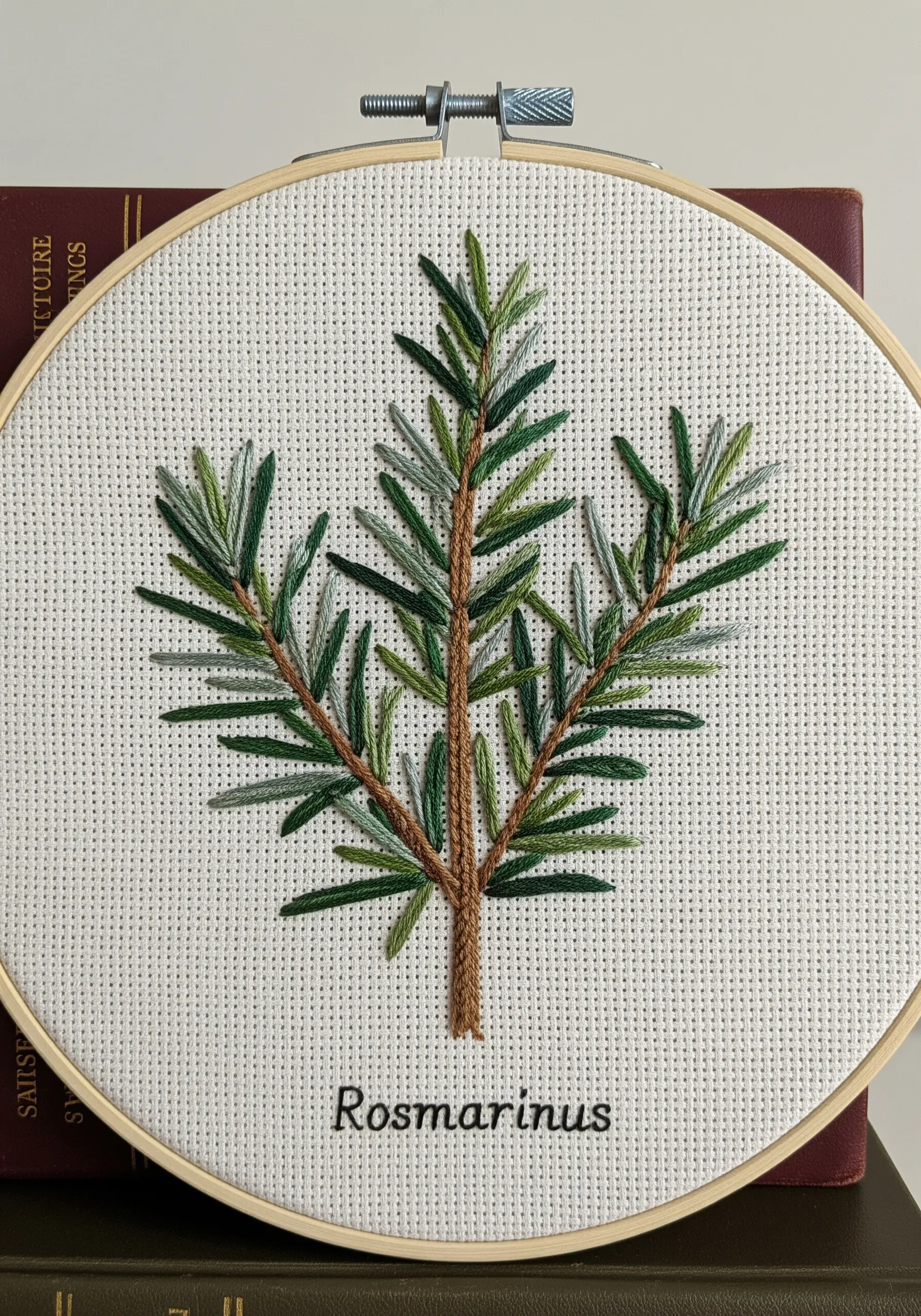 A sprig of rosemary embroidered with straight stitches in various green shades on Aida cloth.