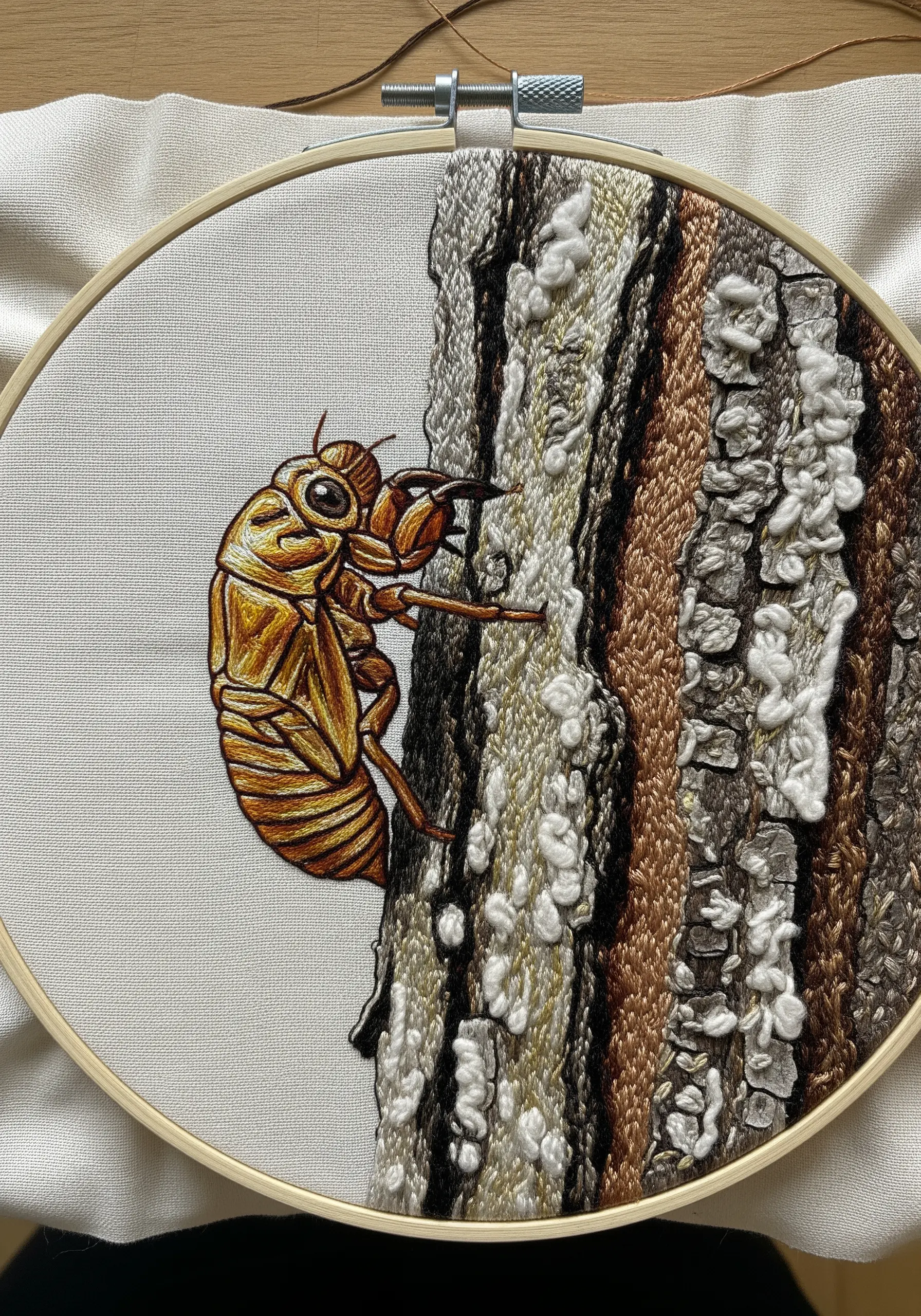 Embroidery of a cicada on a tree with highly textured turkey work for the bark.