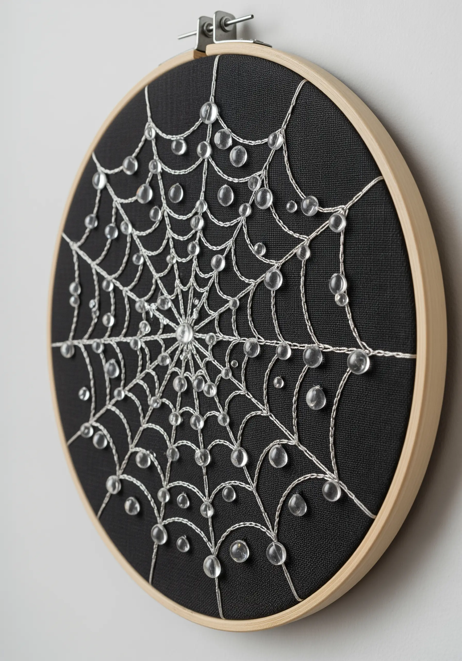An embroidered spiderweb on black fabric, with clear glass beads that look like dewdrops.