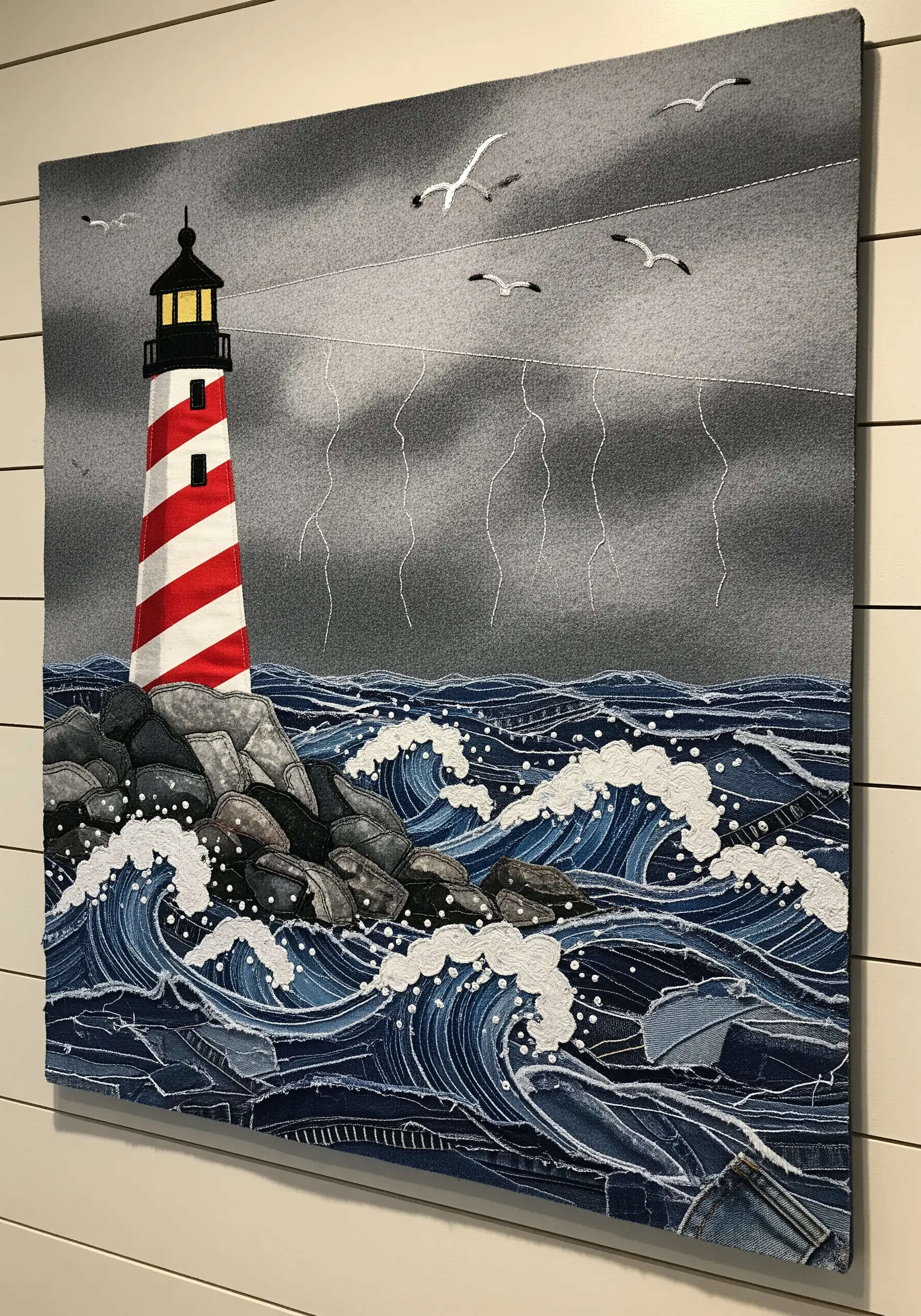 Fabric collage of a lighthouse with a stormy sea made from layered denim scraps