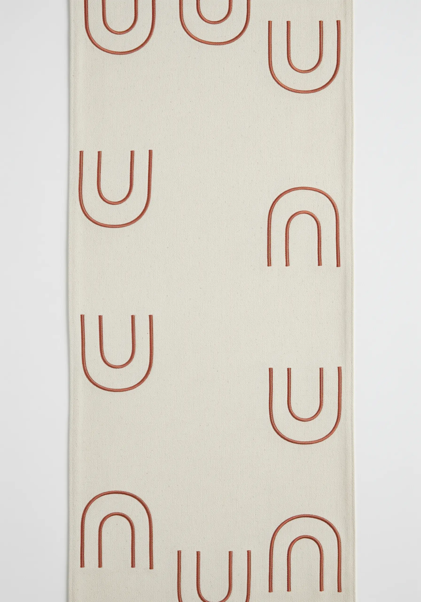 A repeating pattern of minimalist, rust-colored arches stitched on a cream table runner.