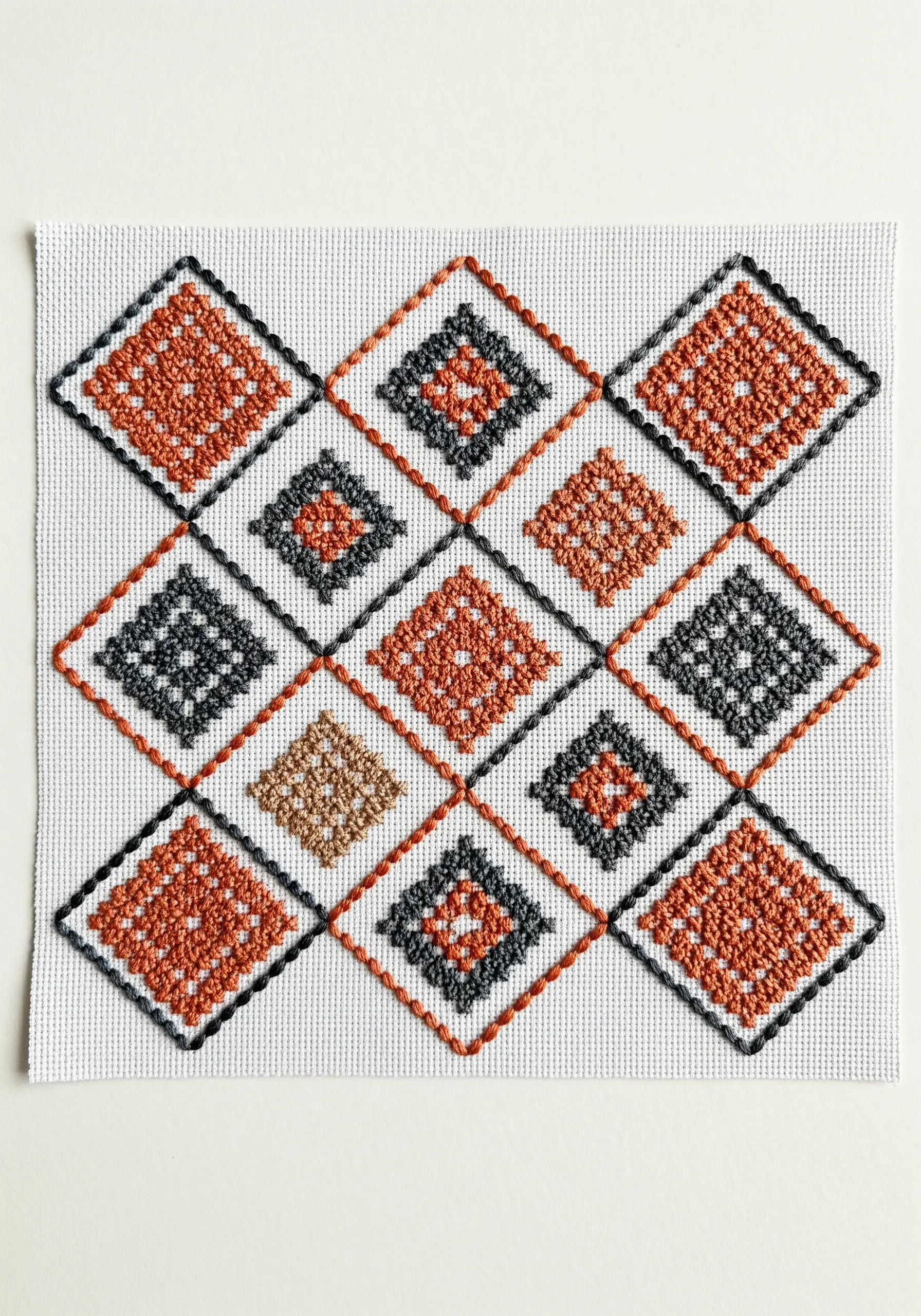 Geometric embroidery with diamond shapes filled with textured stitches in rust and black.