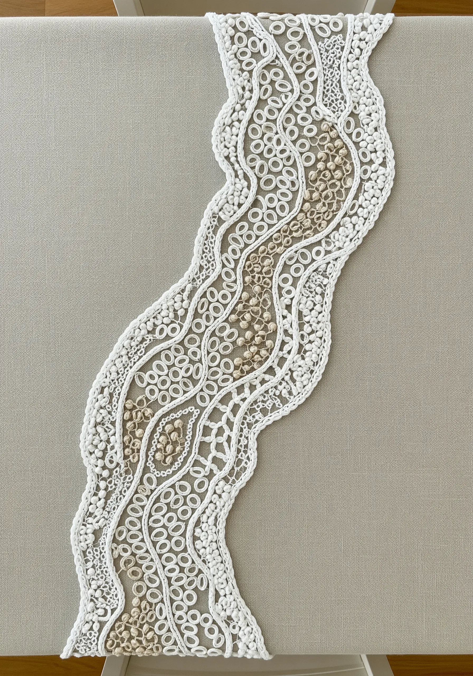 A table runner embroidered with a wavy, river-like pattern using white detached chain stitches and beads.