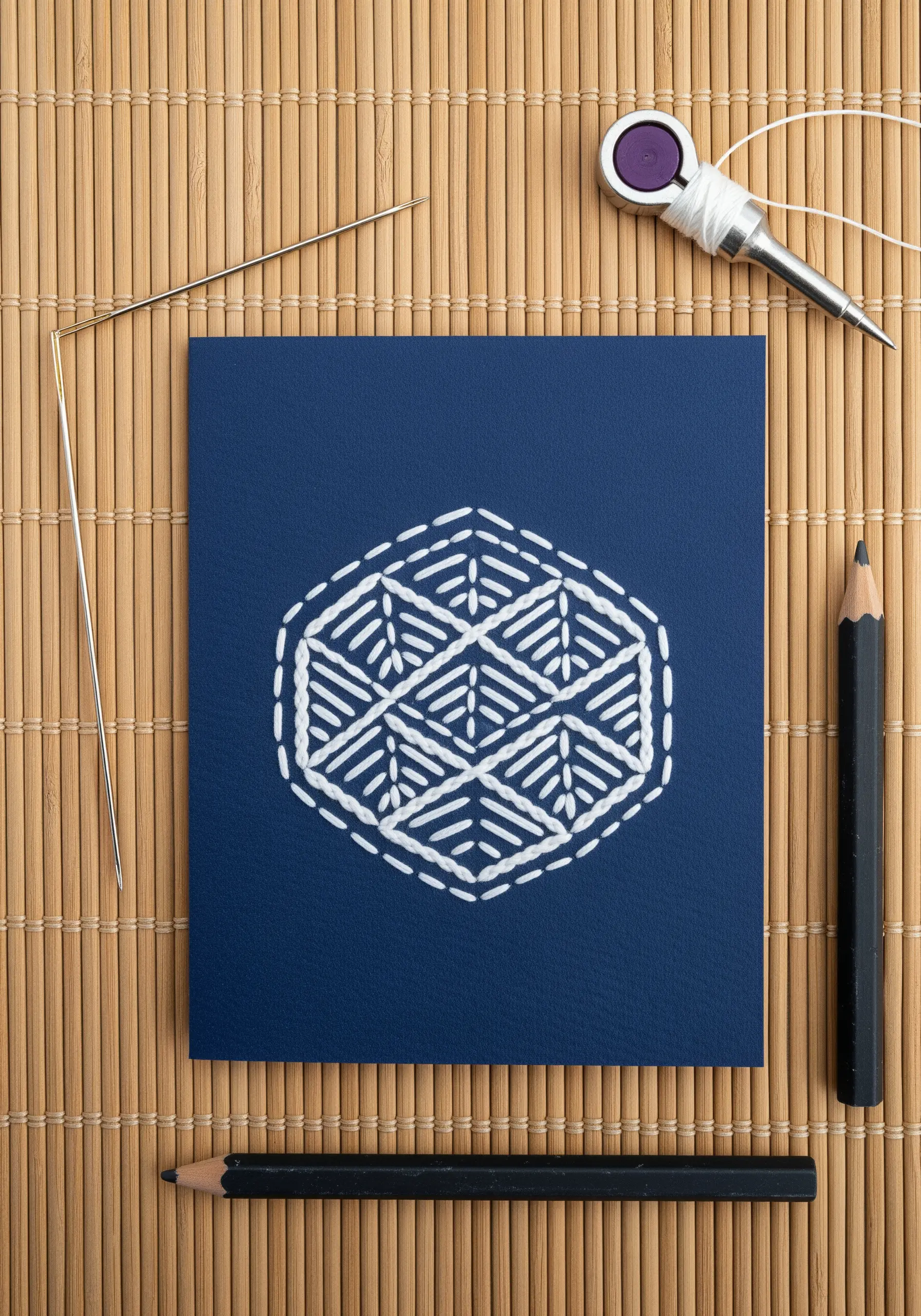 A geometric sashiko pattern stitched with thick white thread on dark blue cardstock.