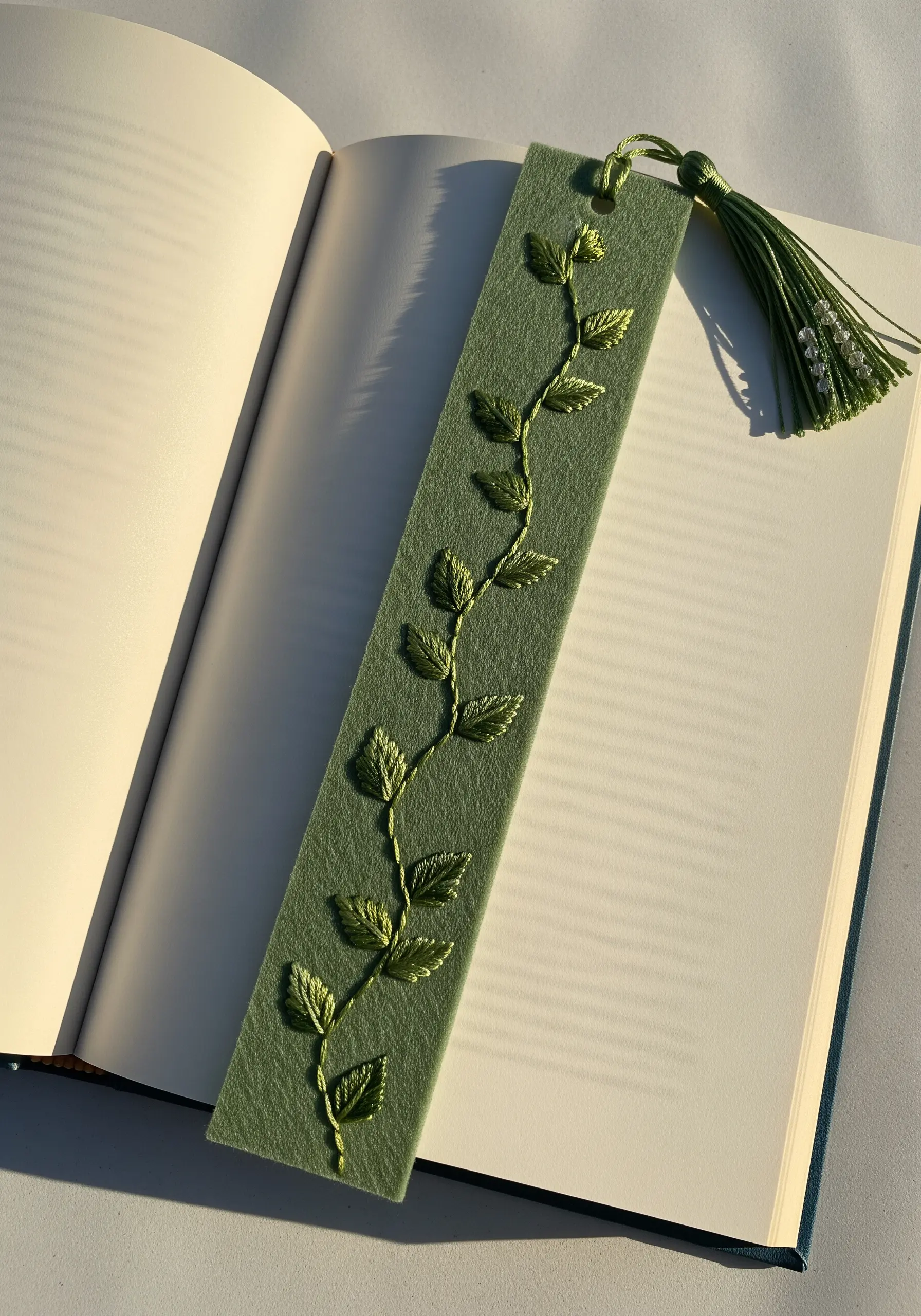 A green felt bookmark with an embroidered vine and shaded leaves.