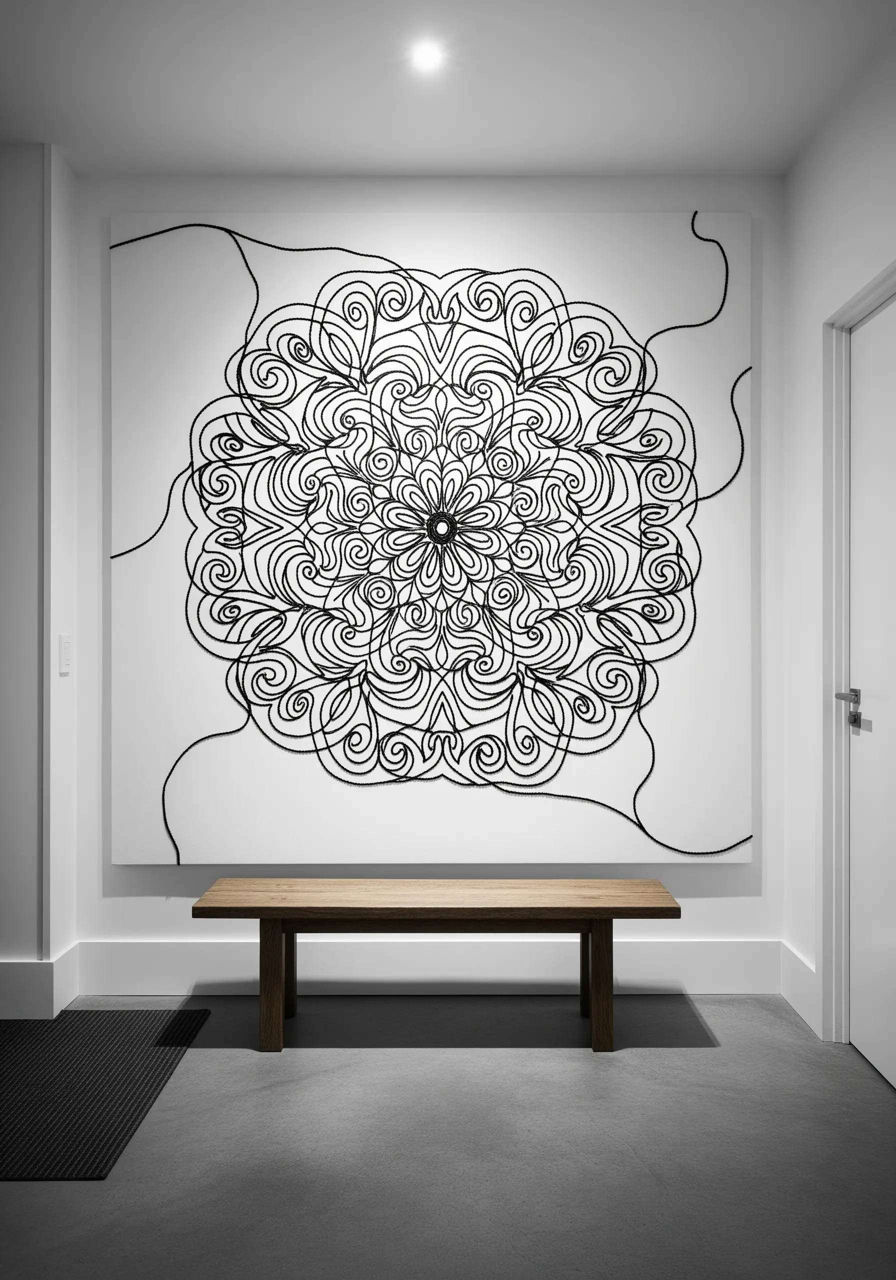 A massive white canvas with a bold, black yarn mandala in a minimalist hallway.
