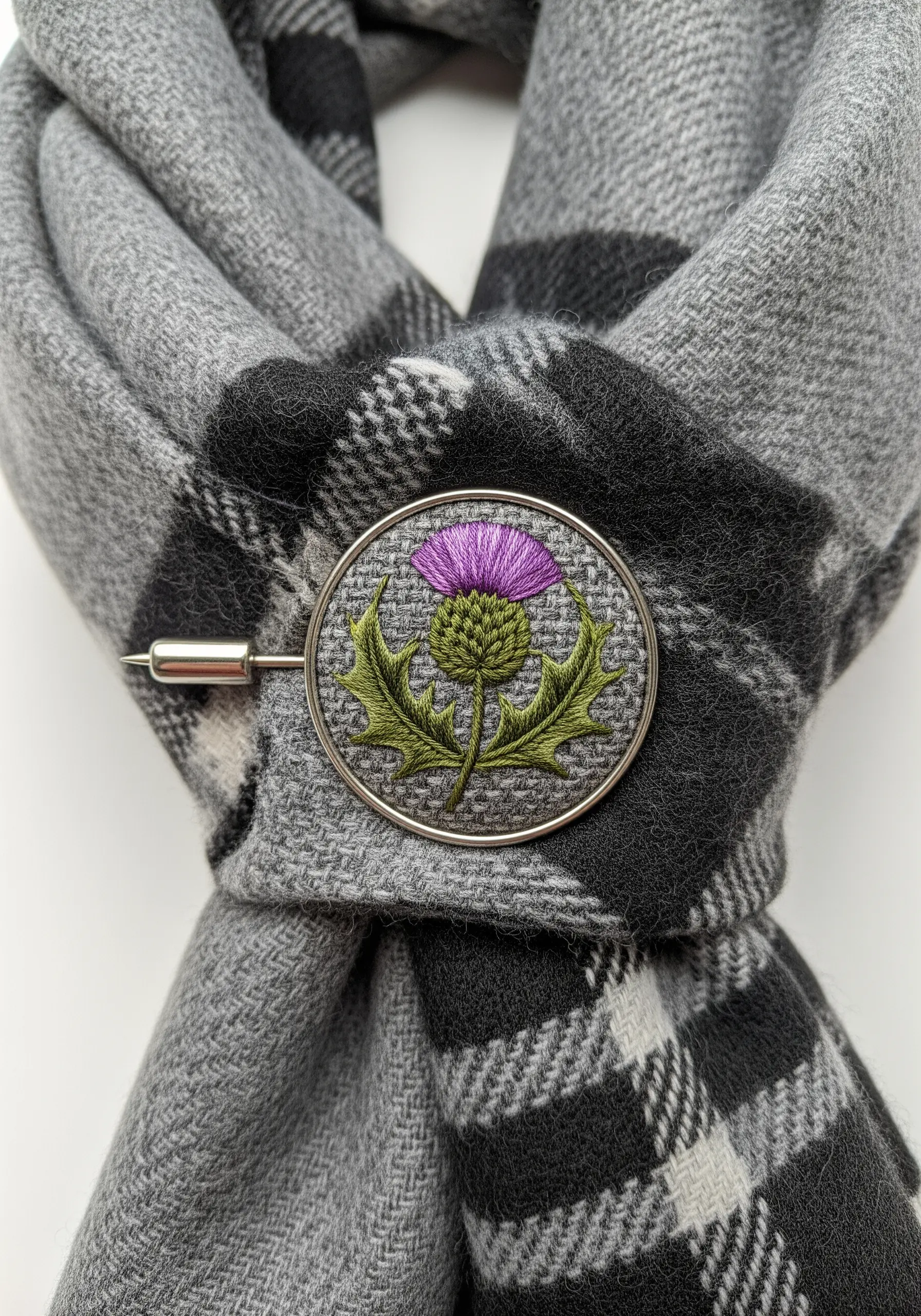 An embroidered Scottish thistle with a textured purple top and spiky green leaves on a scarf pin.