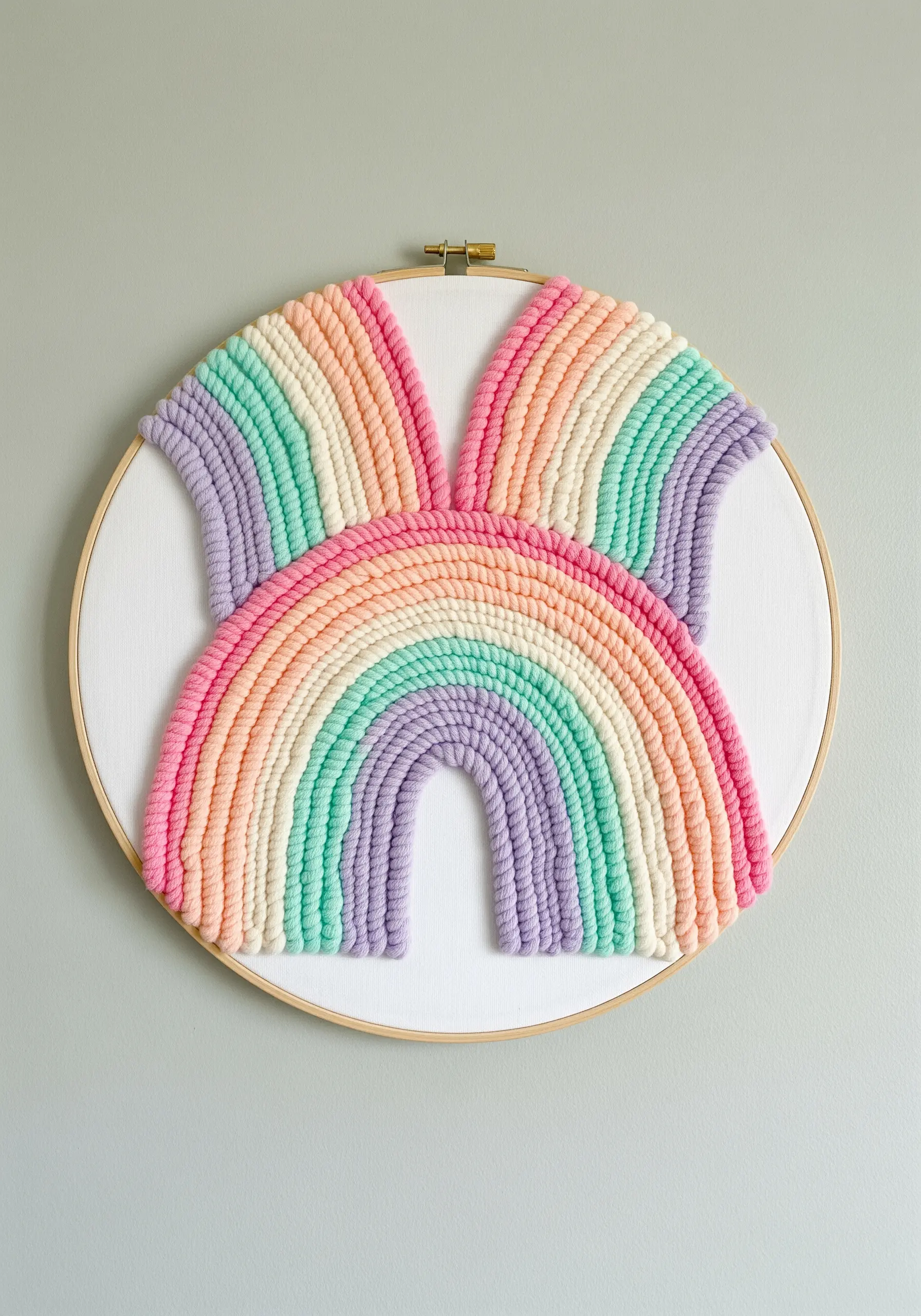 Sculptural rainbow arcs made from yarn-wrapped cording stitched onto a white canvas hoop.