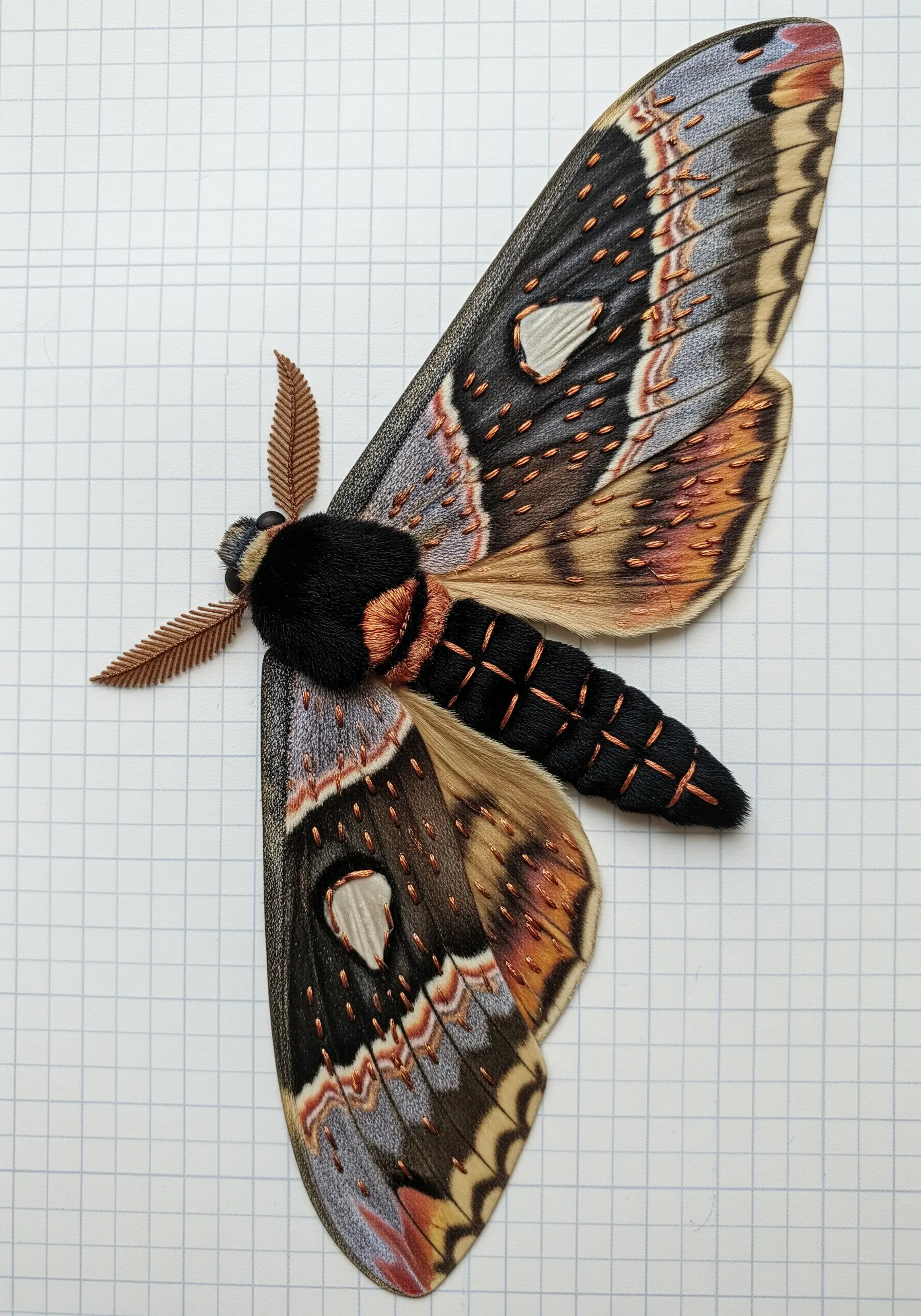 A paper moth collage with a raised, 3D body created with padded satin stitch.