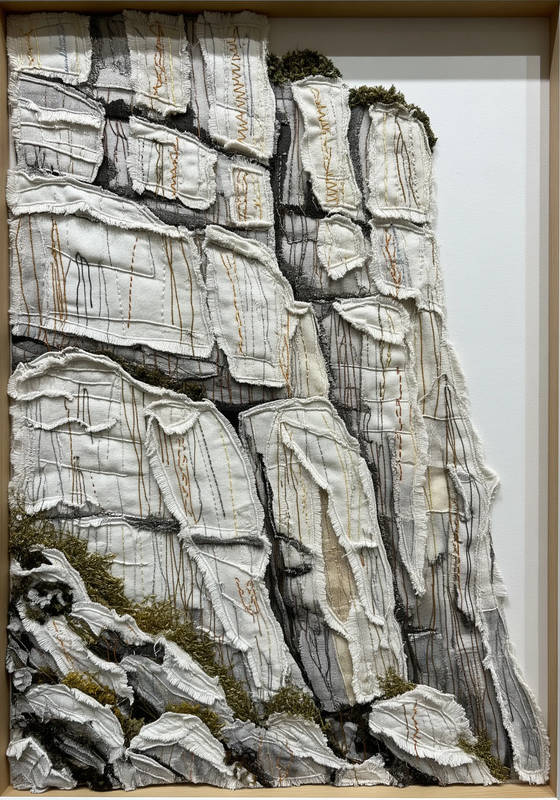 Framed 3D textile art depicting a rocky cliff face with layered fabric and stitching.
