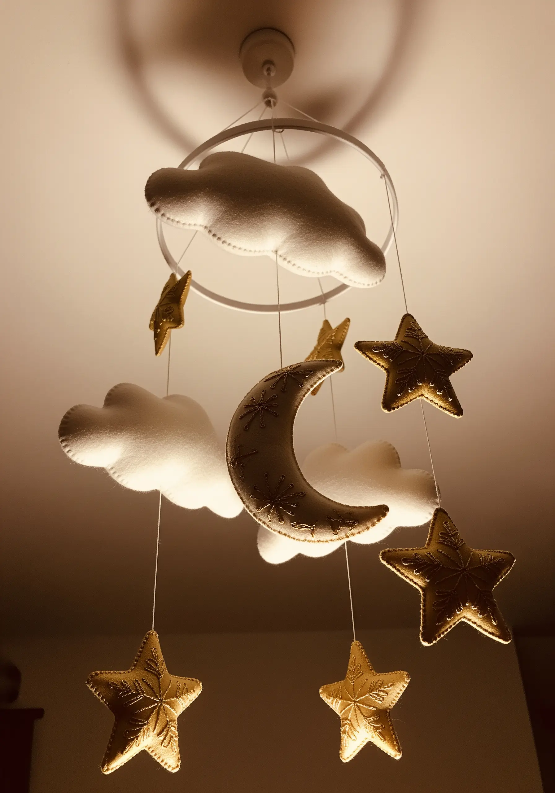 A handmade nursery mobile featuring soft, embroidered felt clouds, a crescent moon, and stars.
