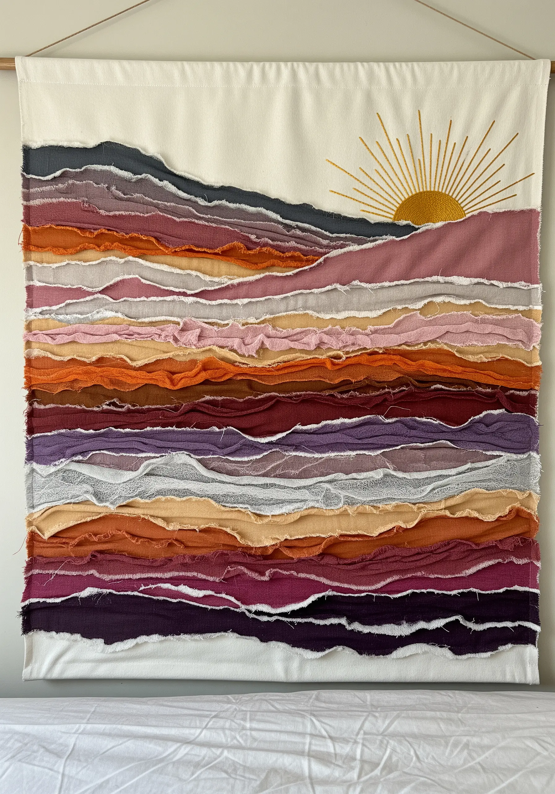 A wall hanging of a sunset landscape made from layered, torn strips of fabric in warm tones.