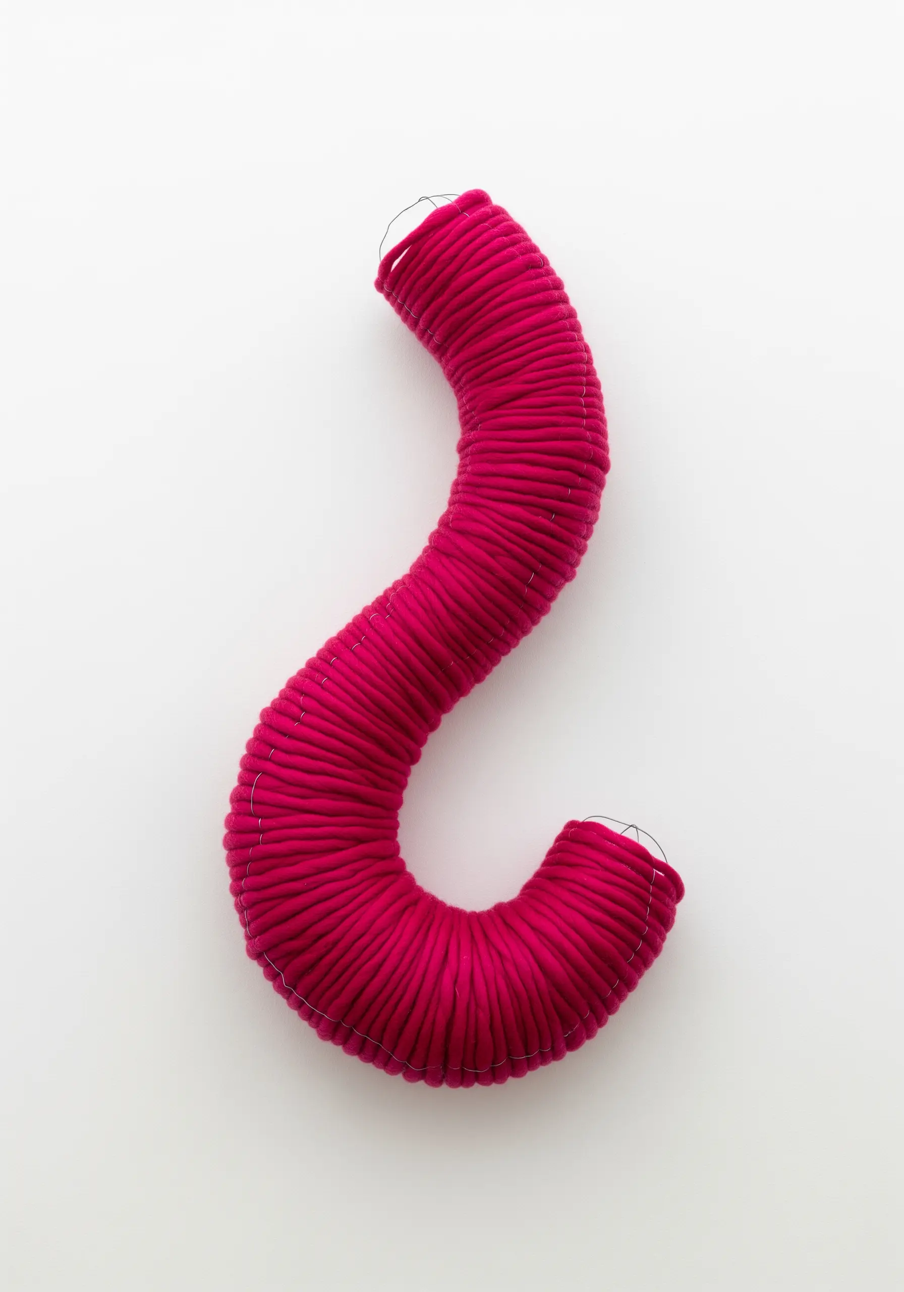 A minimalist, S-shaped wall sculpture made from bright pink yarn wrapped around a wire frame.