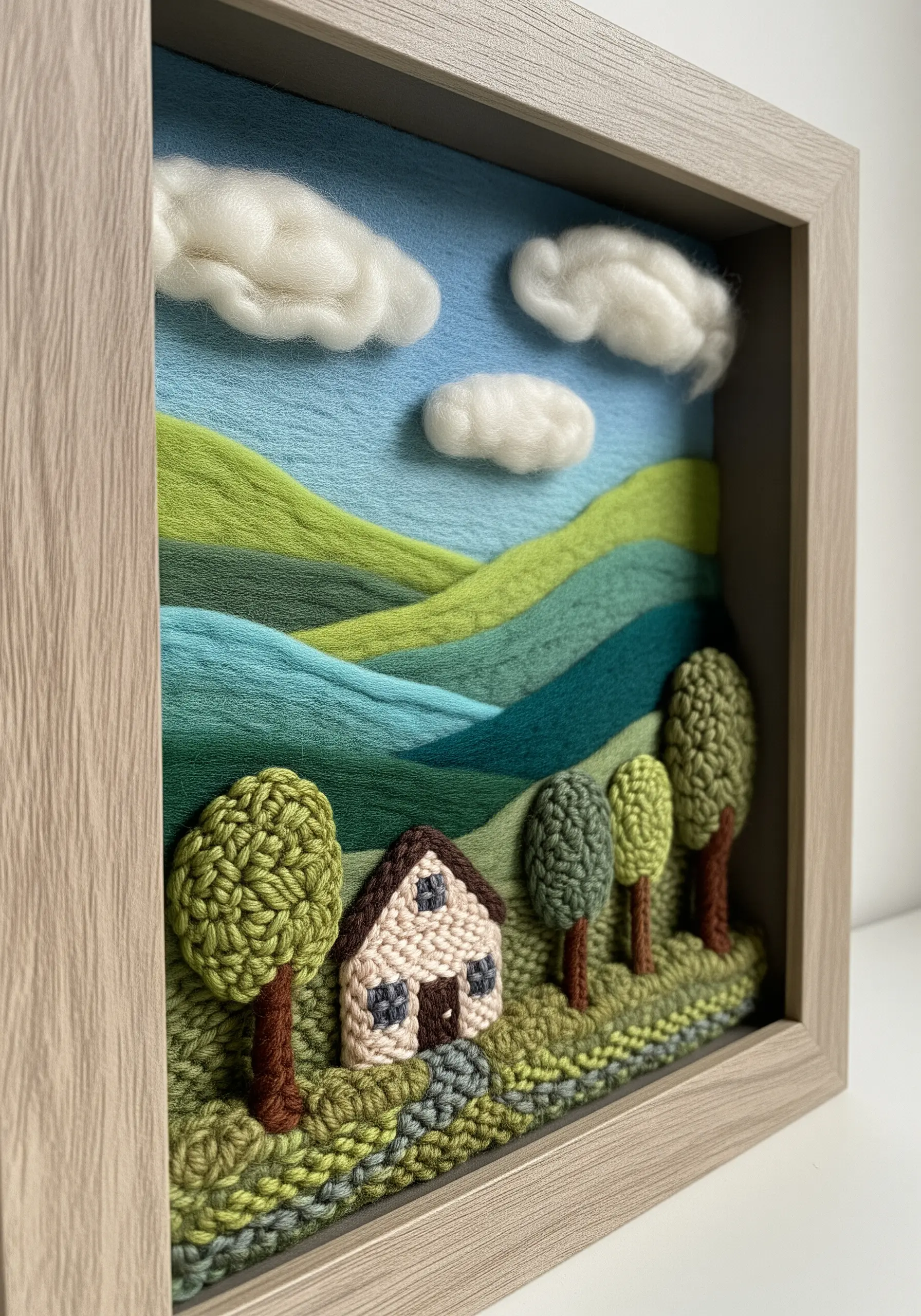 A framed 3D landscape made with needle felting and embroidery, featuring hills and trees.
