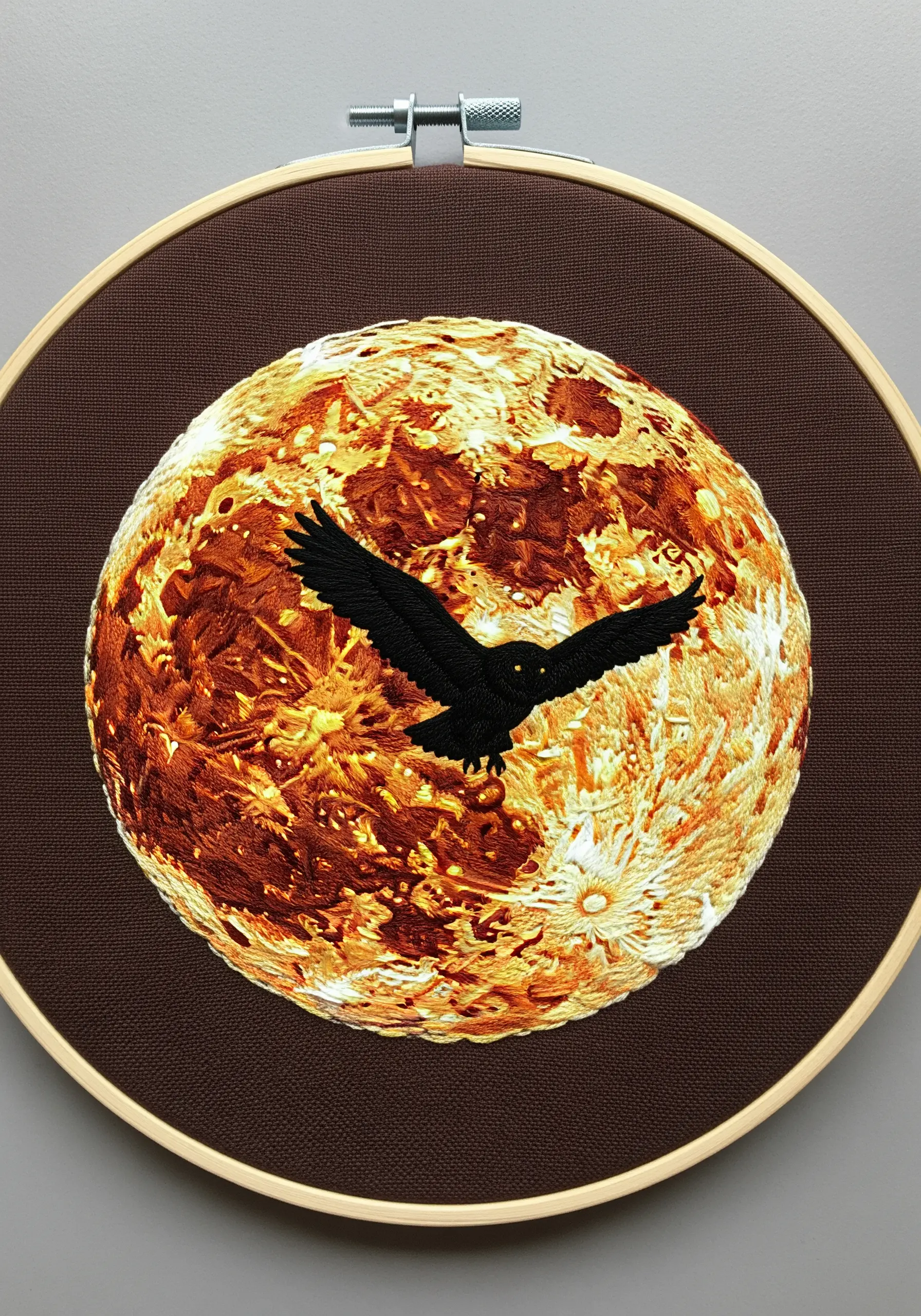 A black owl silhouette flying across a heavily textured, embroidered planet in fiery orange and gold.