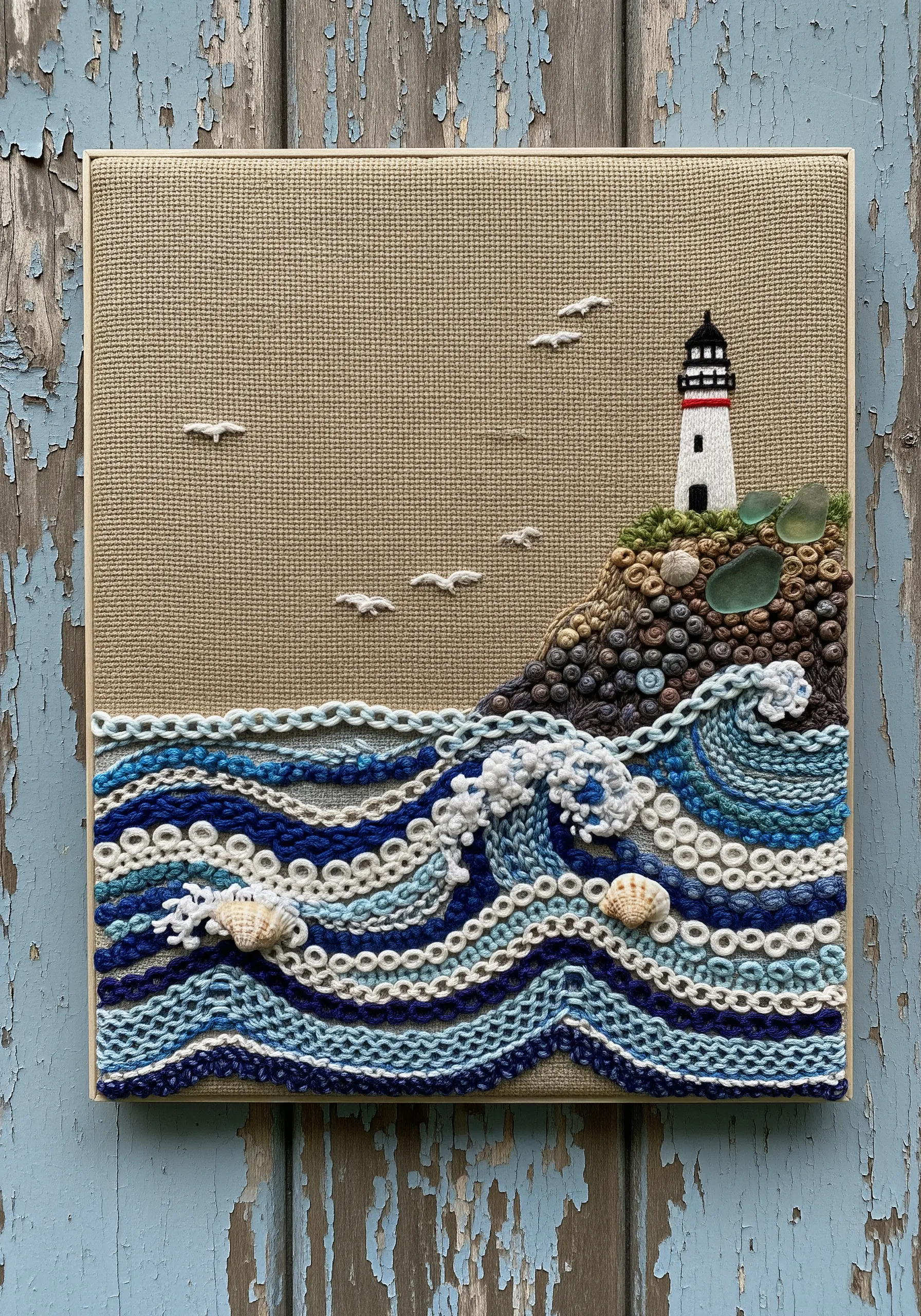 Textured embroidery of a lighthouse and ocean waves with added shells and sea glass