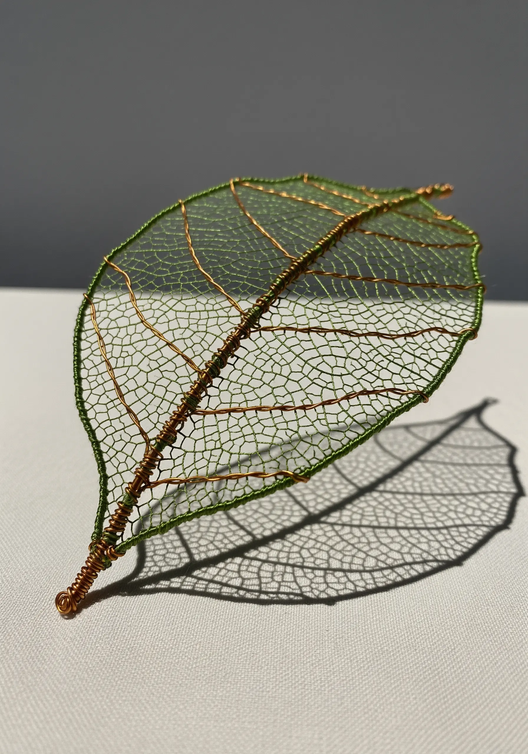 A delicate, translucent leaf made from green thread stitched over a copper wire frame.