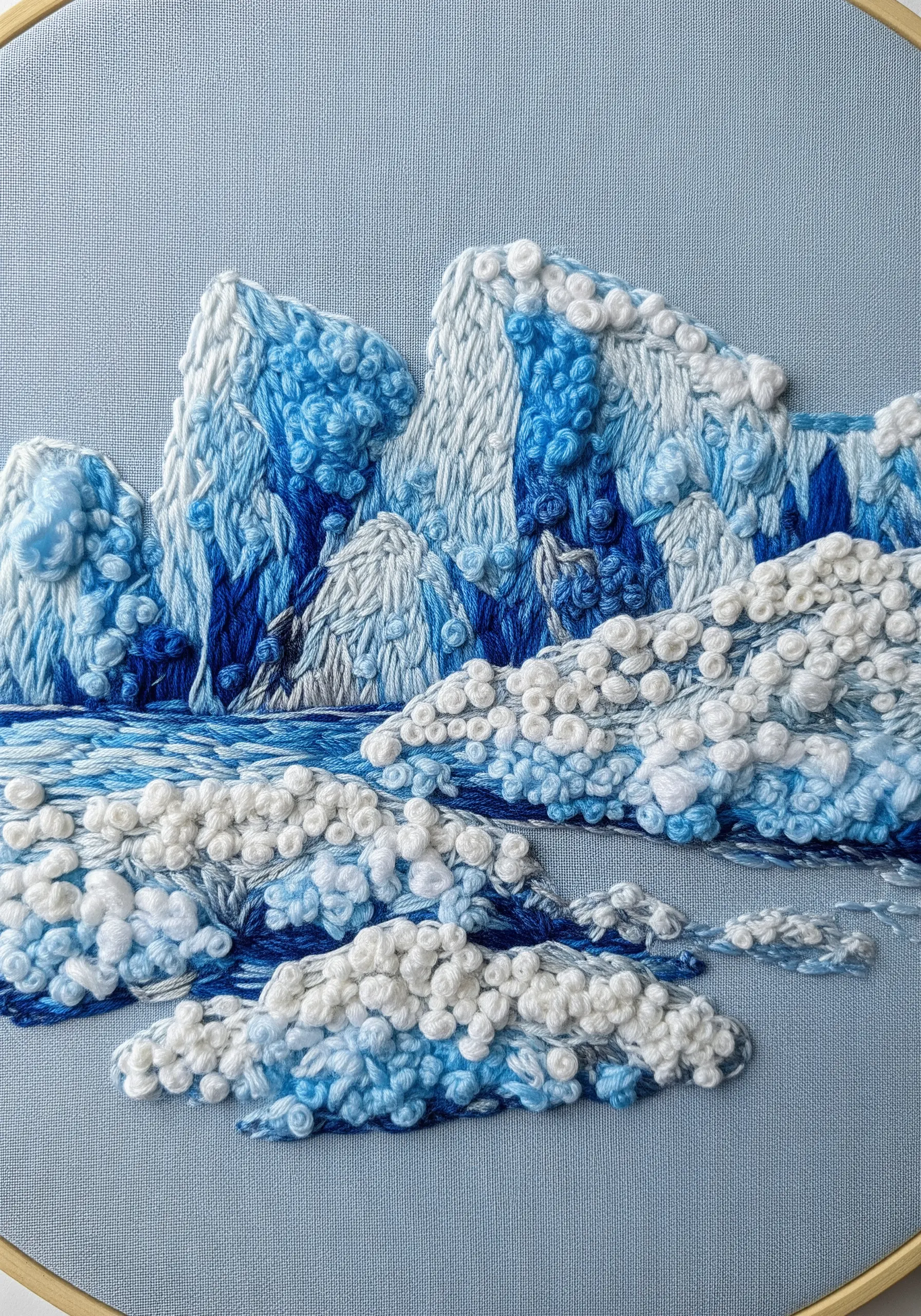 Highly textured blue and white embroidery of snowy mountains using French knots.