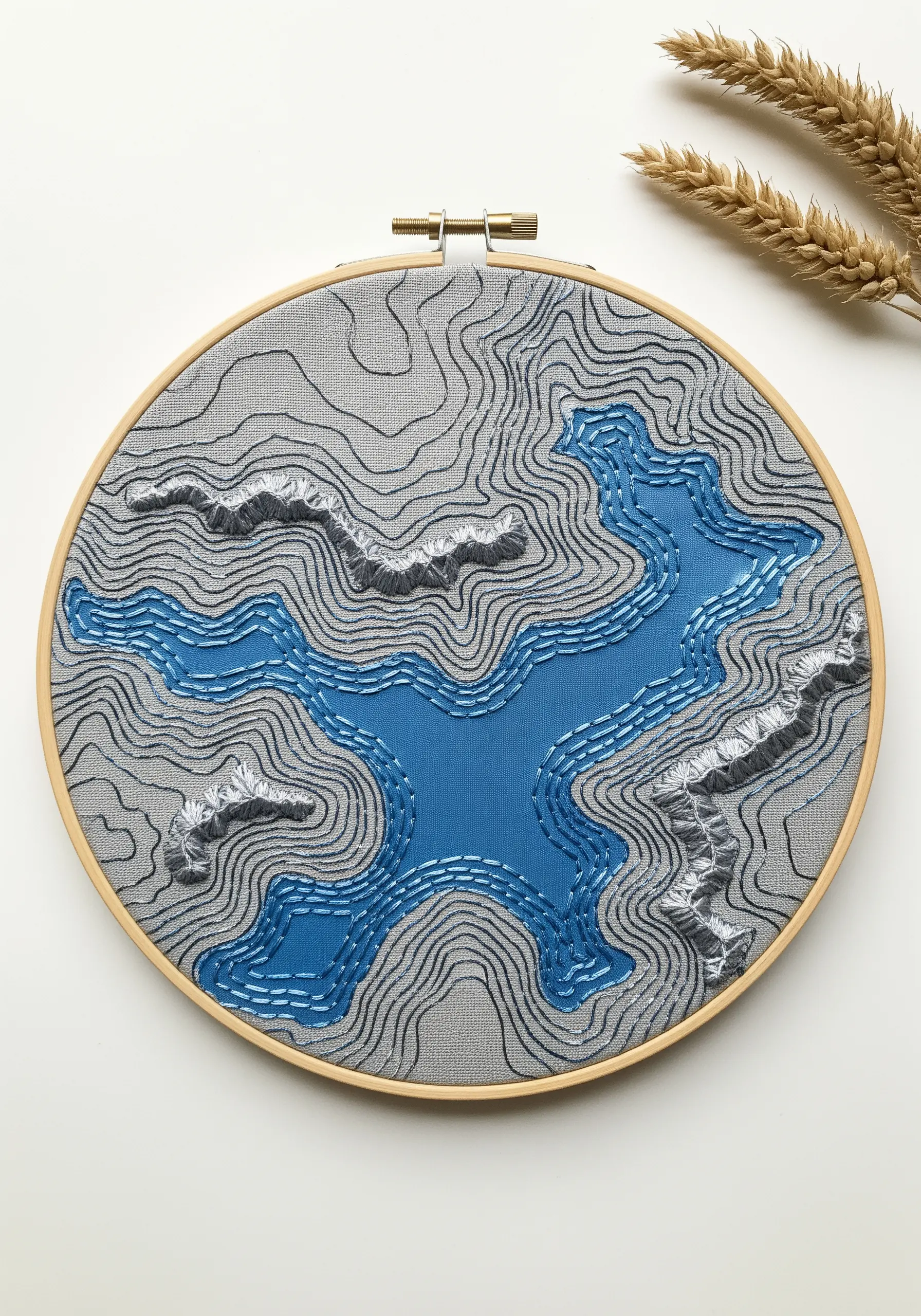 An embroidered topographical map in a hoop with raised stitches for mountain ranges.