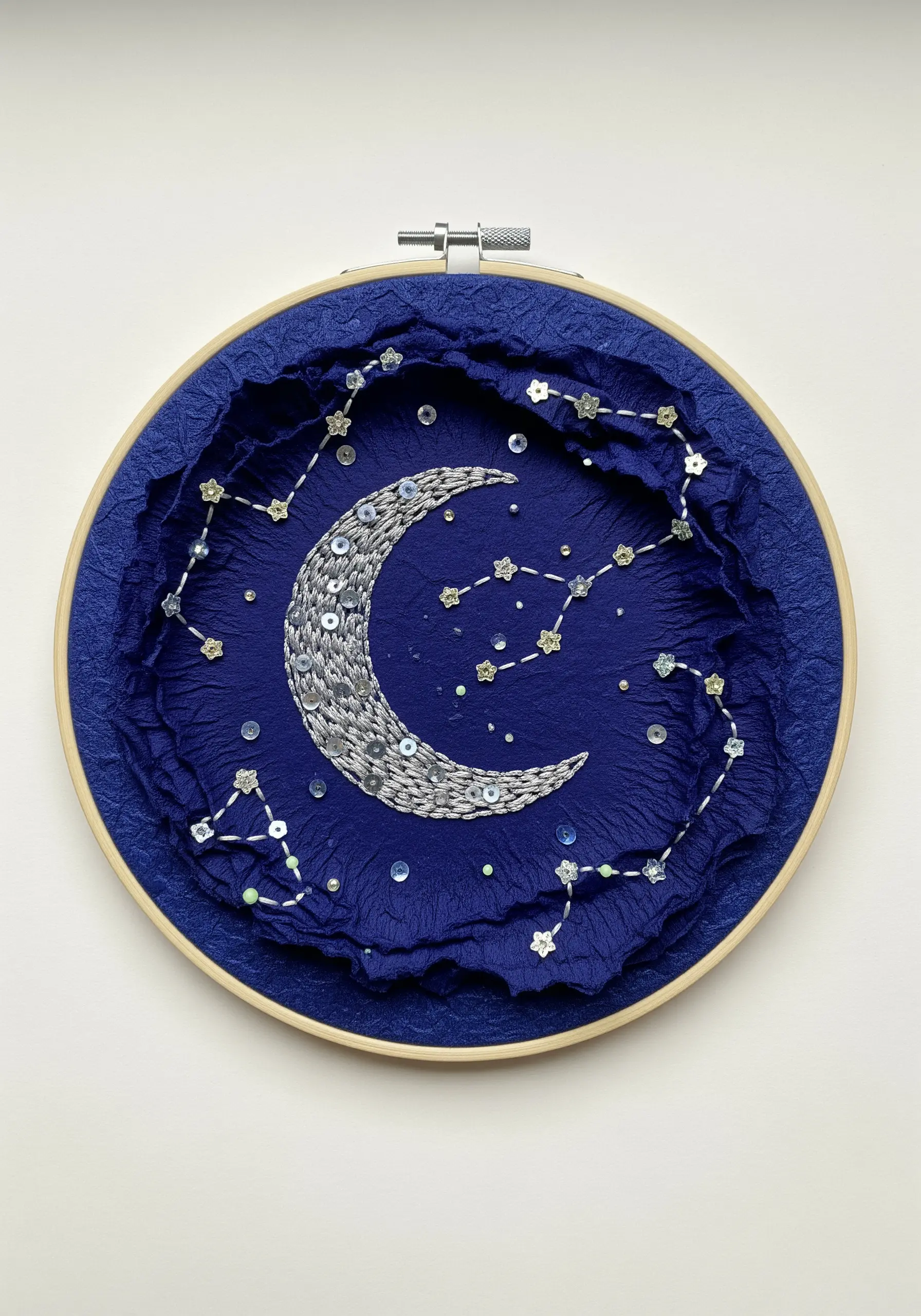 Sequined moon and constellations embroidered on sculpted dark blue paper.