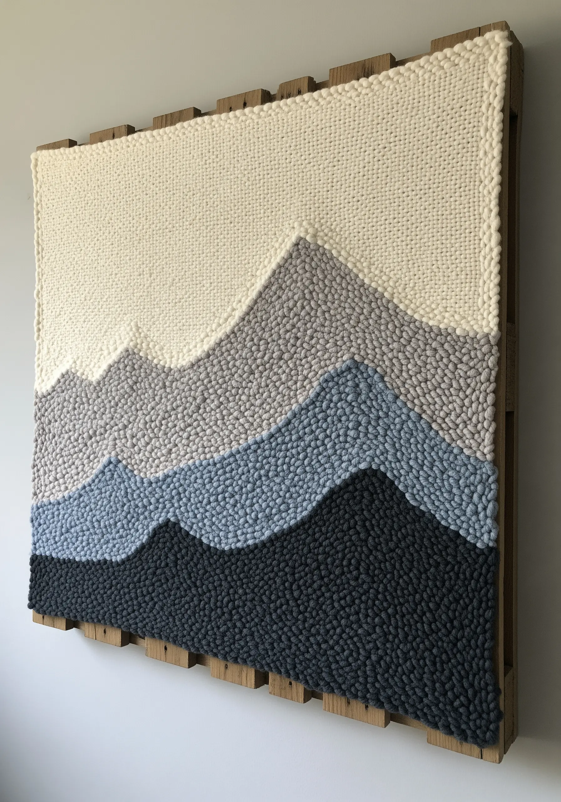 A punch needle wall art piece depicting rolling hills in shades of cream, grey, and blue.