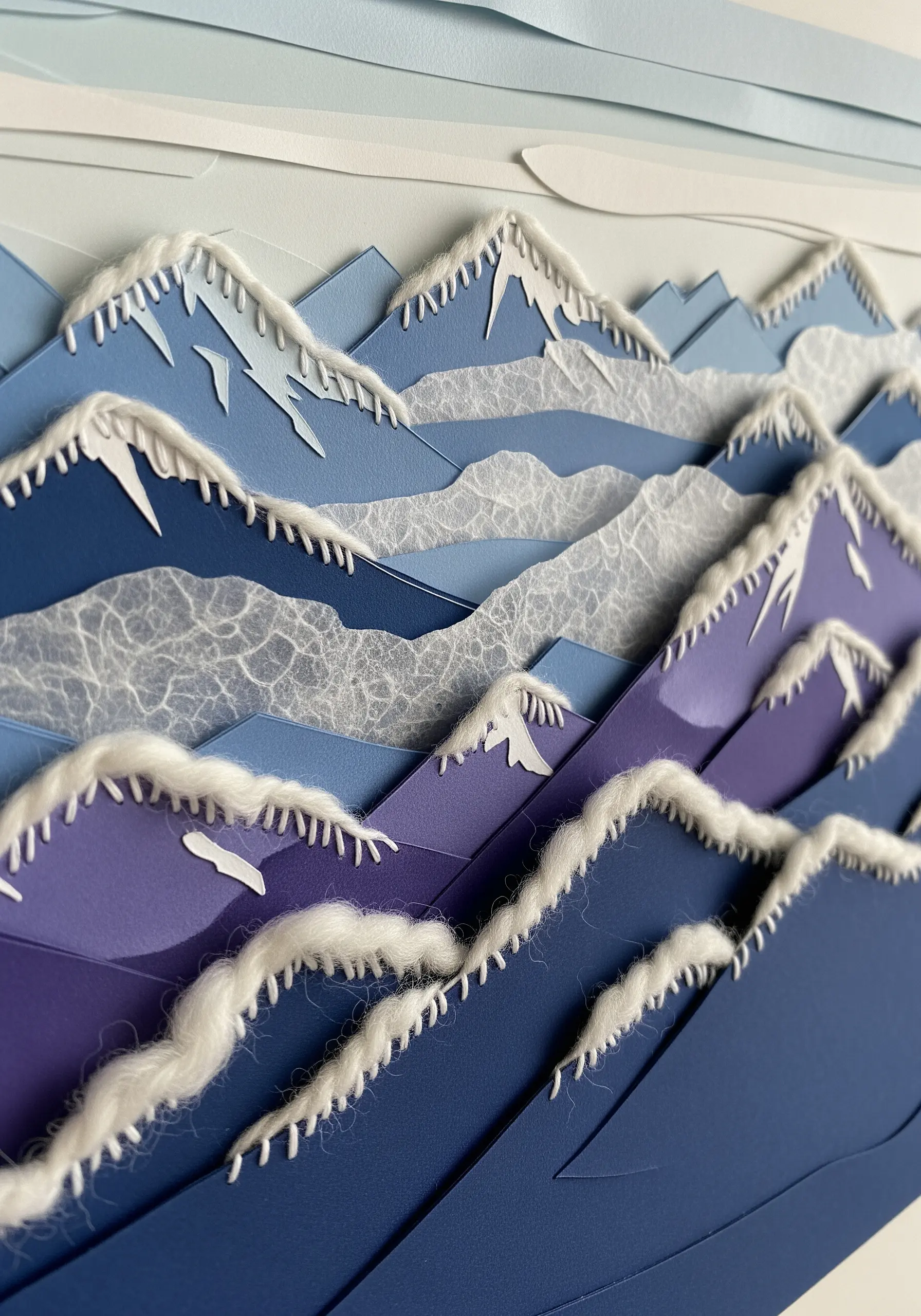 A layered paper mountain range with snowcaps created from thick, fluffy white yarn stitches.