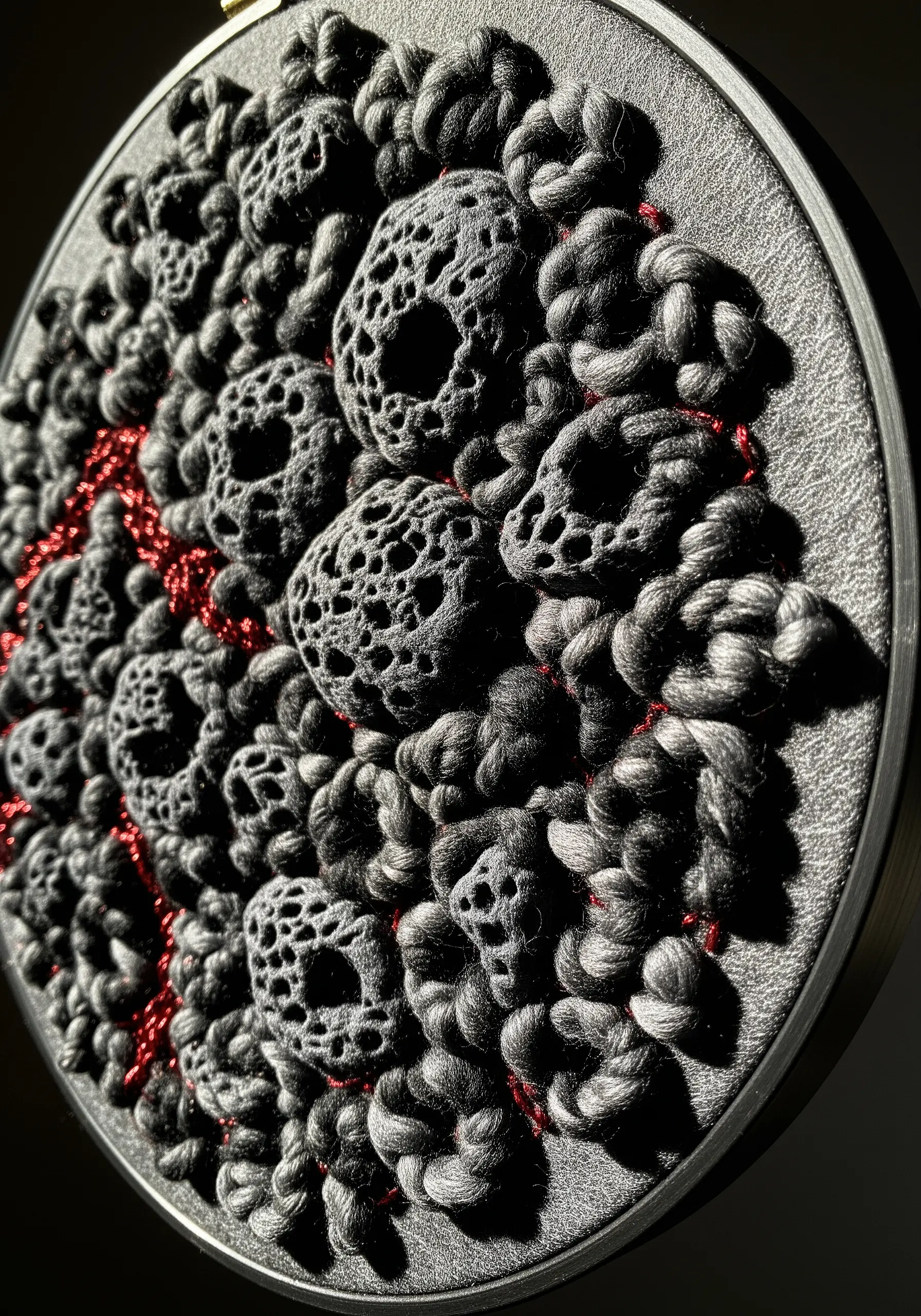 Abstract black embroidery with raised knots and hollow, web-like stitches resembling volcanic rock.