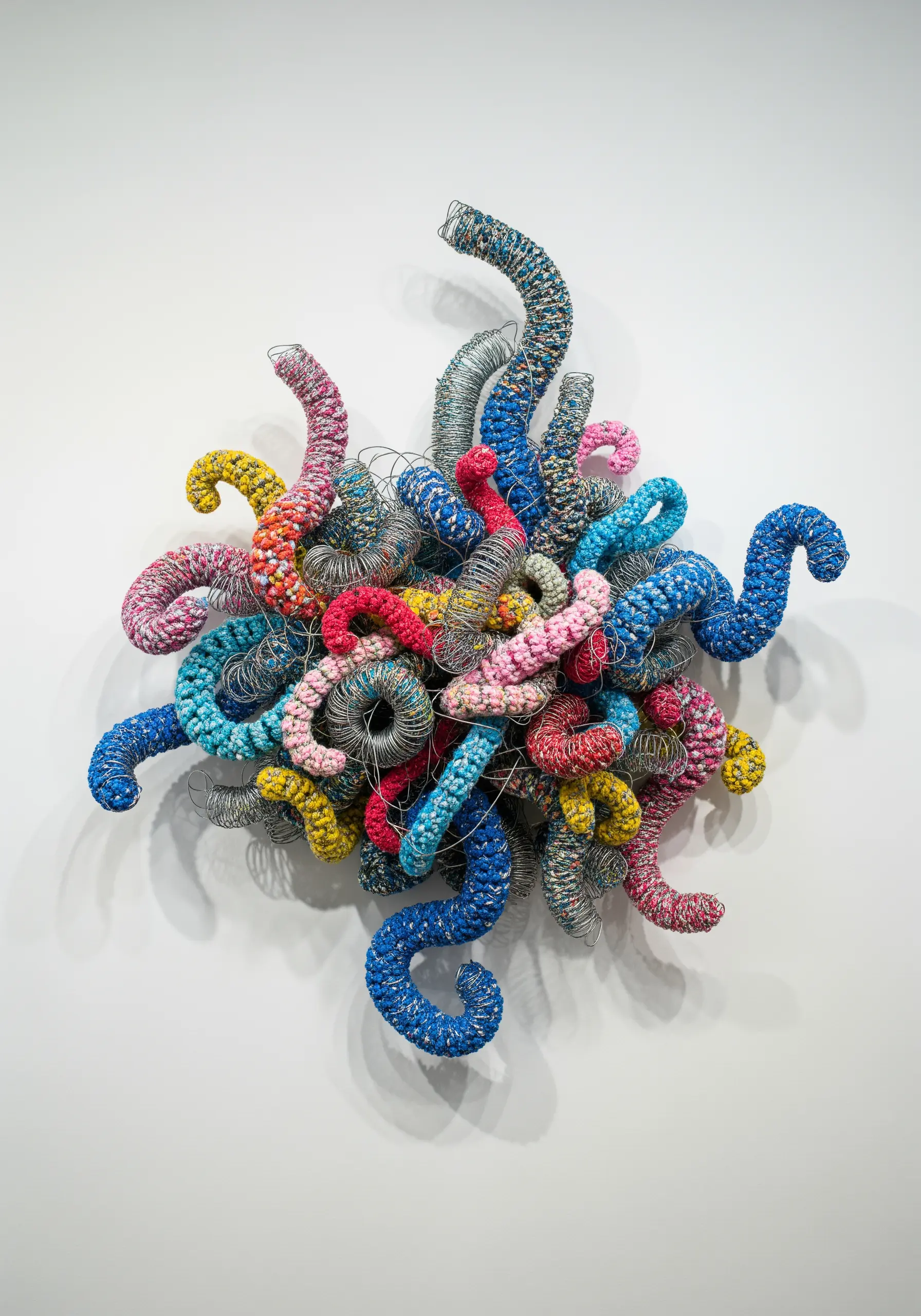 A 3D wall sculpture made of colorful yarn-wrapped wires bent into chaotic, organic shapes.