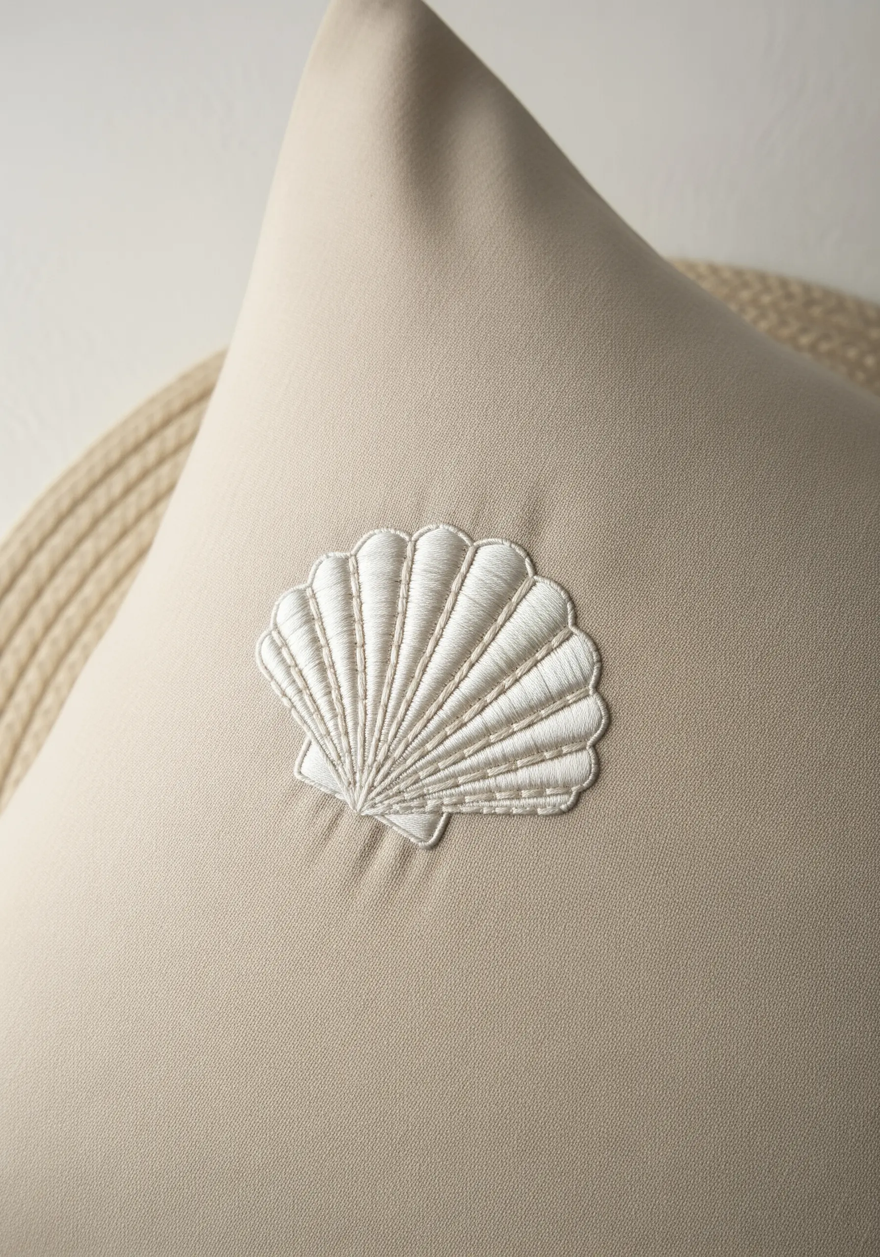 A white embroidered seashell on a beige pillow, using directional satin stitch for texture.