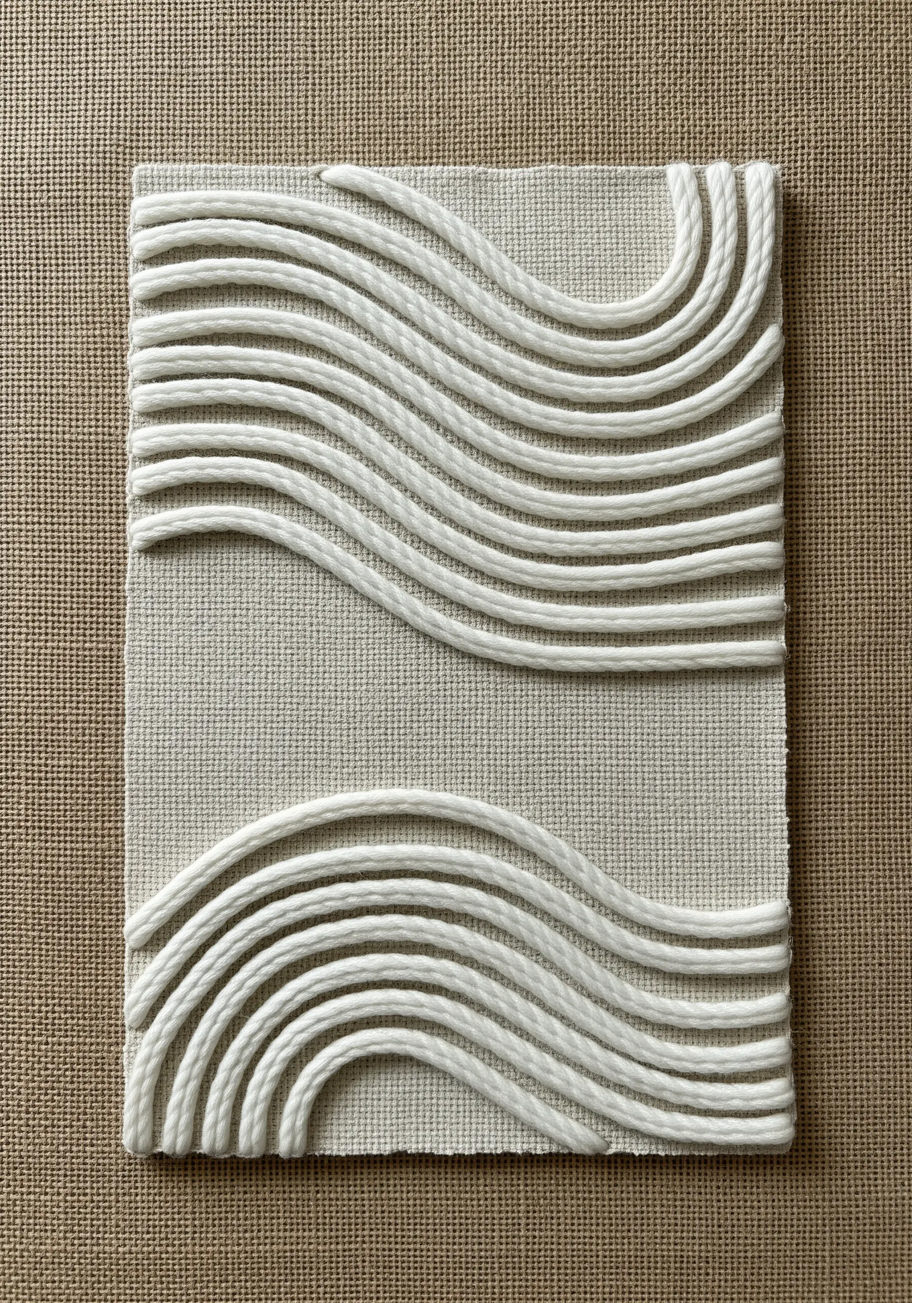 Sculptural white waves made from wrapped cording on a neutral canvas background.