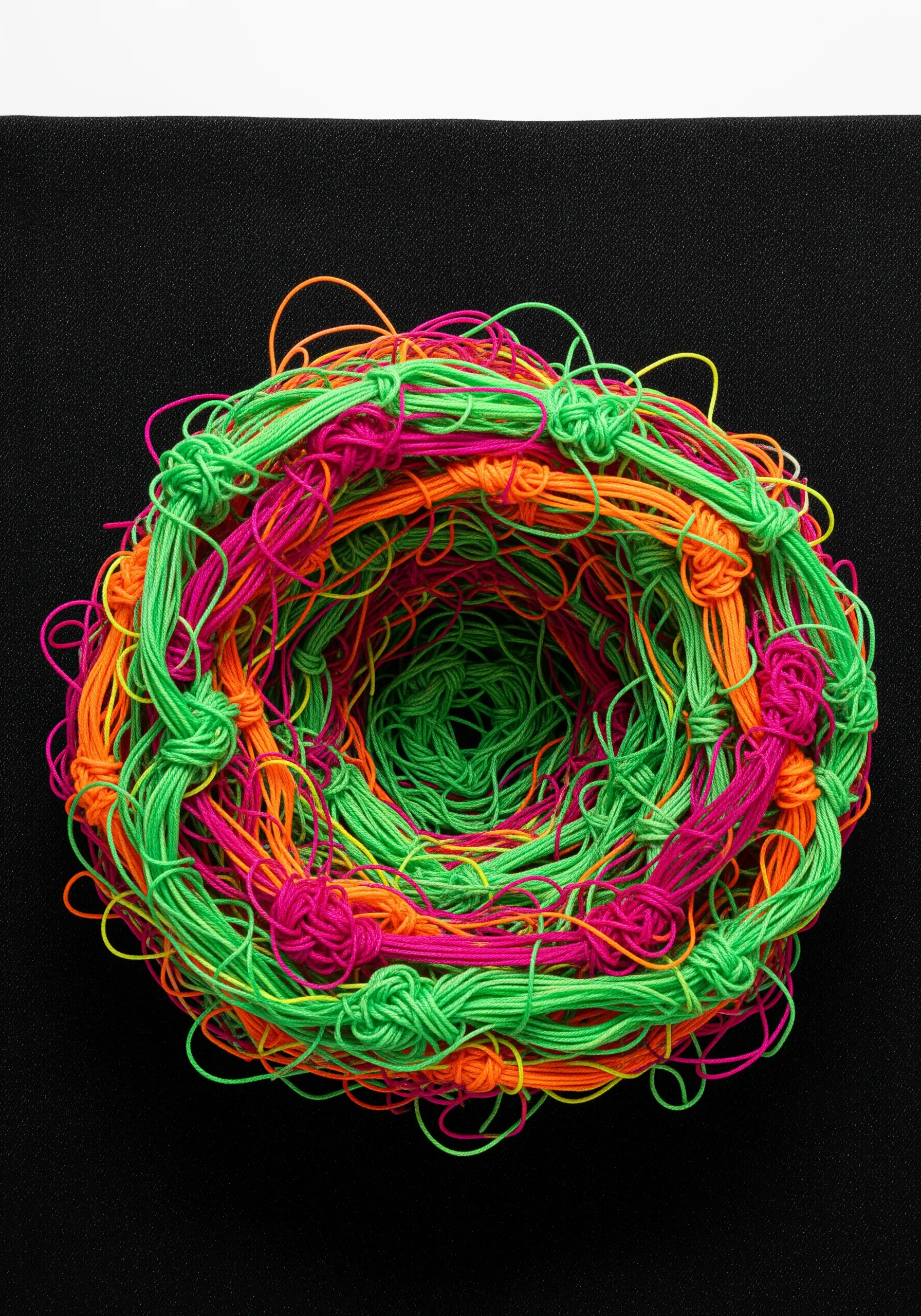 A 3D woven structure of knotted neon green, pink, and orange cords.