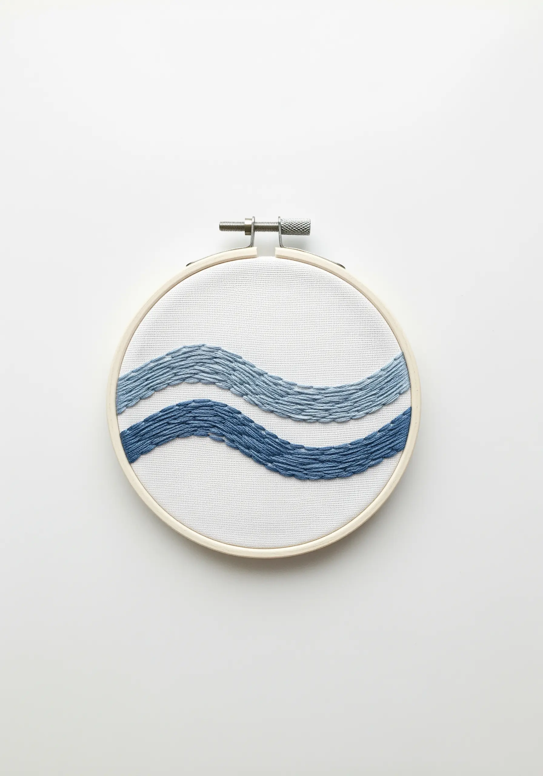 Two abstract waves in shades of blue using satin stitch on white fabric.