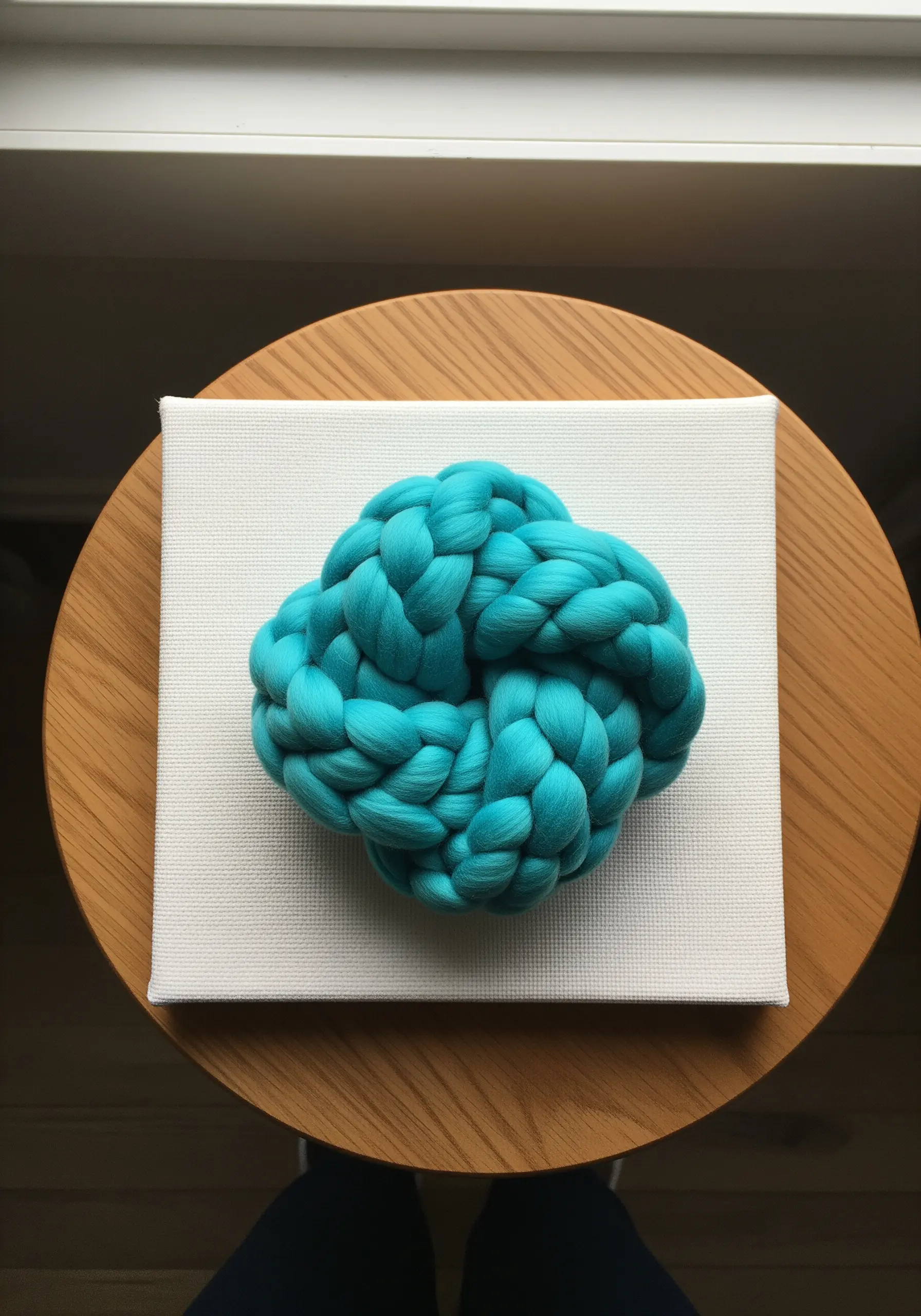 A large, bright turquoise chunky yarn knot mounted on a plain white canvas.