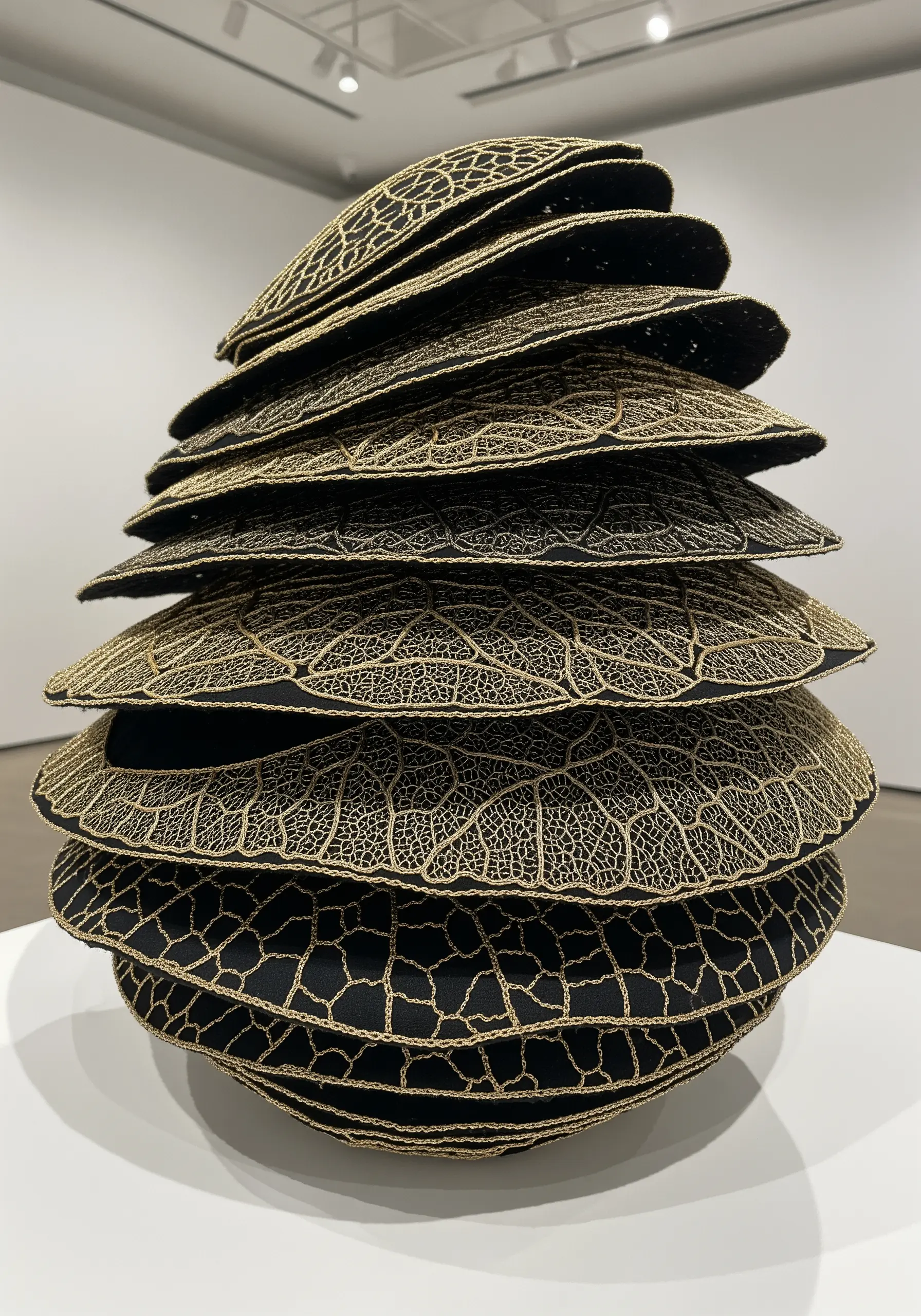 A stacked 3D sculpture of black pods covered in a gold thread lace pattern.