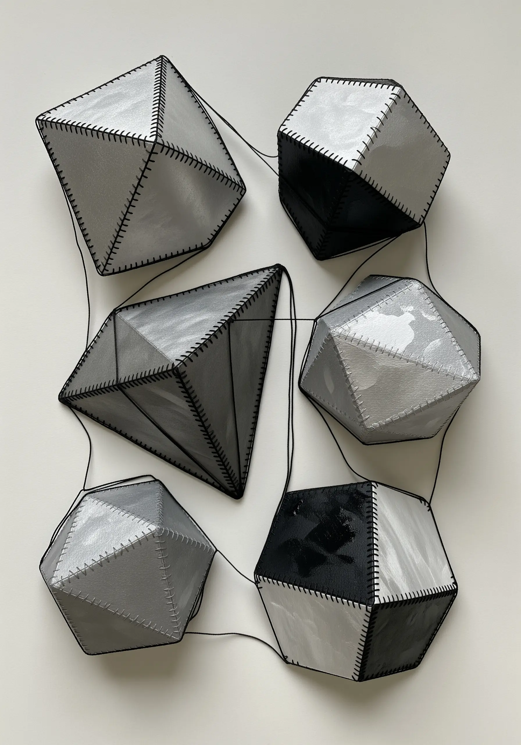 3D geometric paper sculptures held together with visible black stitching.
