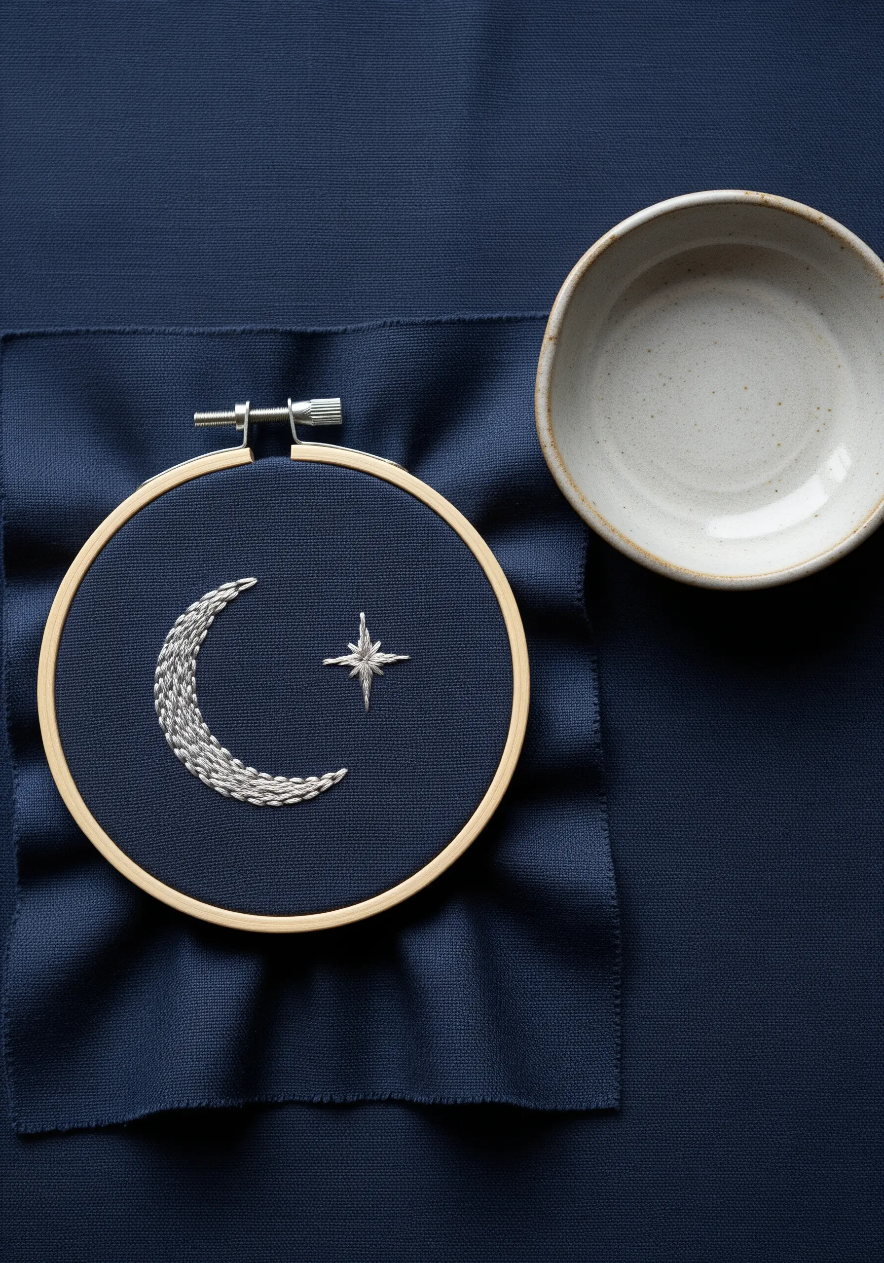 A crescent moon filled with silver chain stitch next to a star on navy fabric.